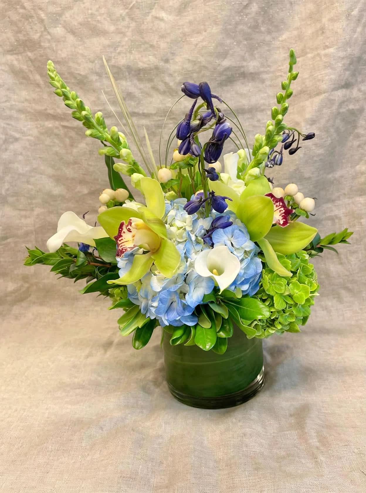 Blue hydrangeas with green orchids and white calla lilies in a green vase