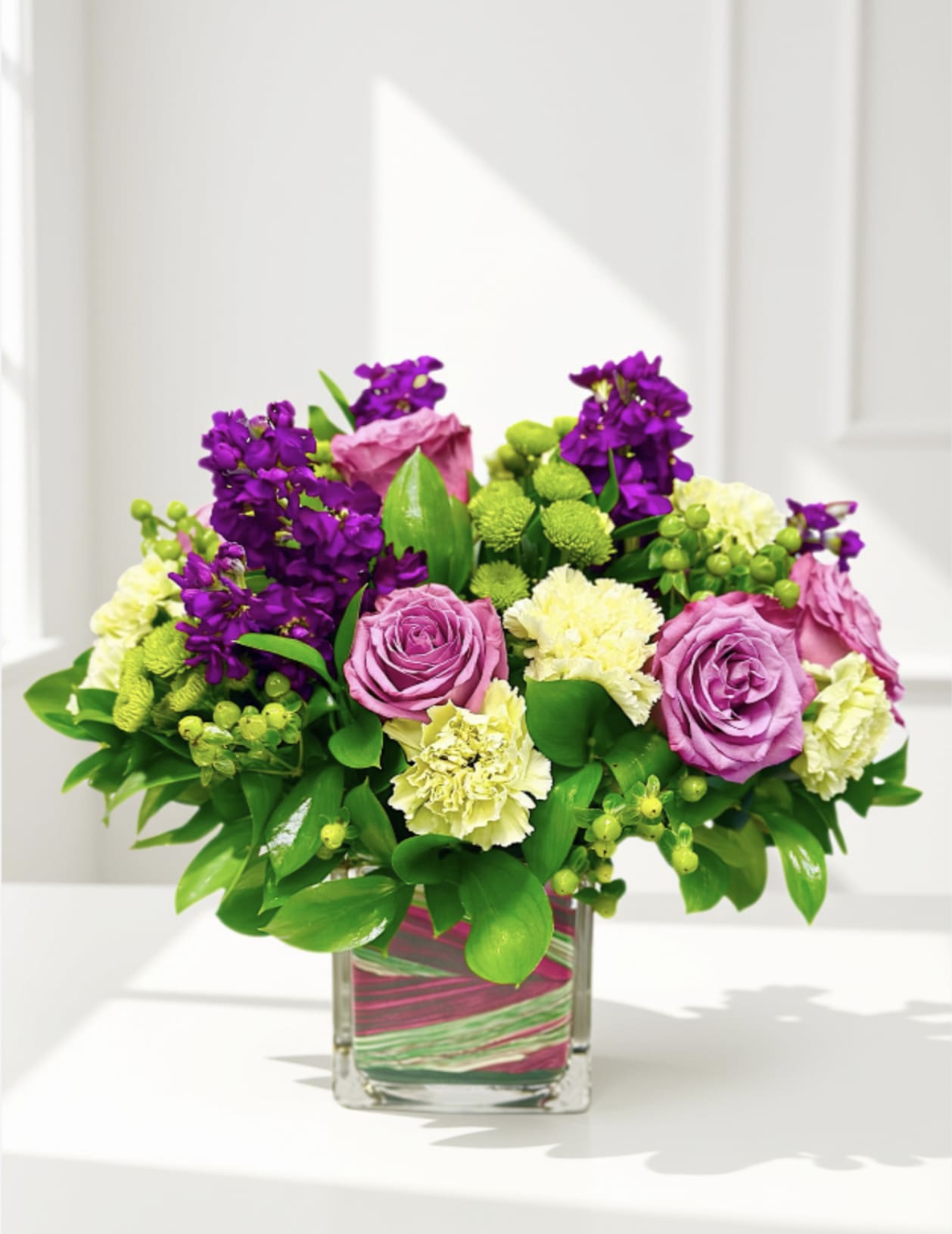 Pink roses and purple flowers arranged in a square glass vase