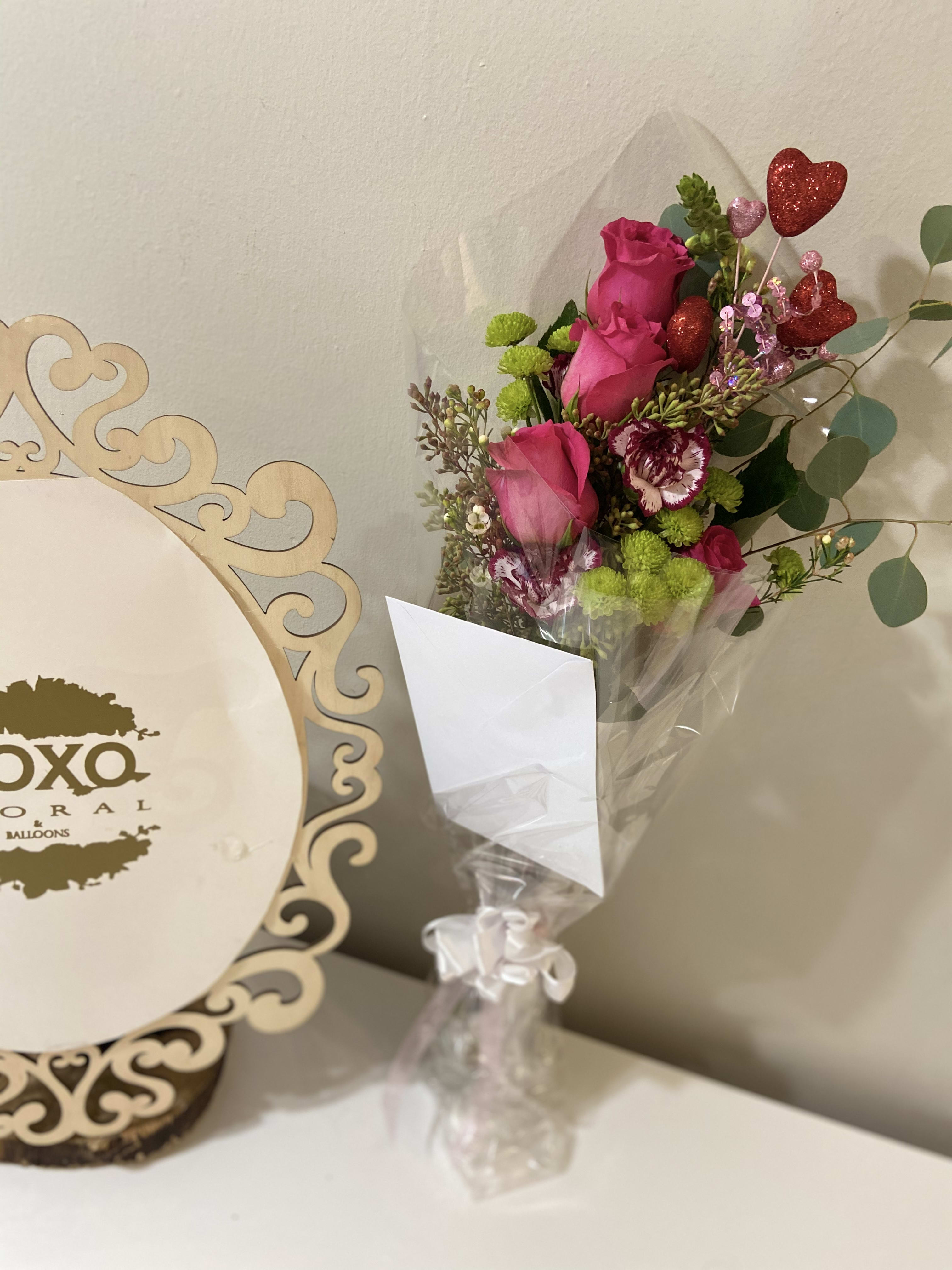 Bouquet of pink roses and green button mums with heart picks in a clear vase