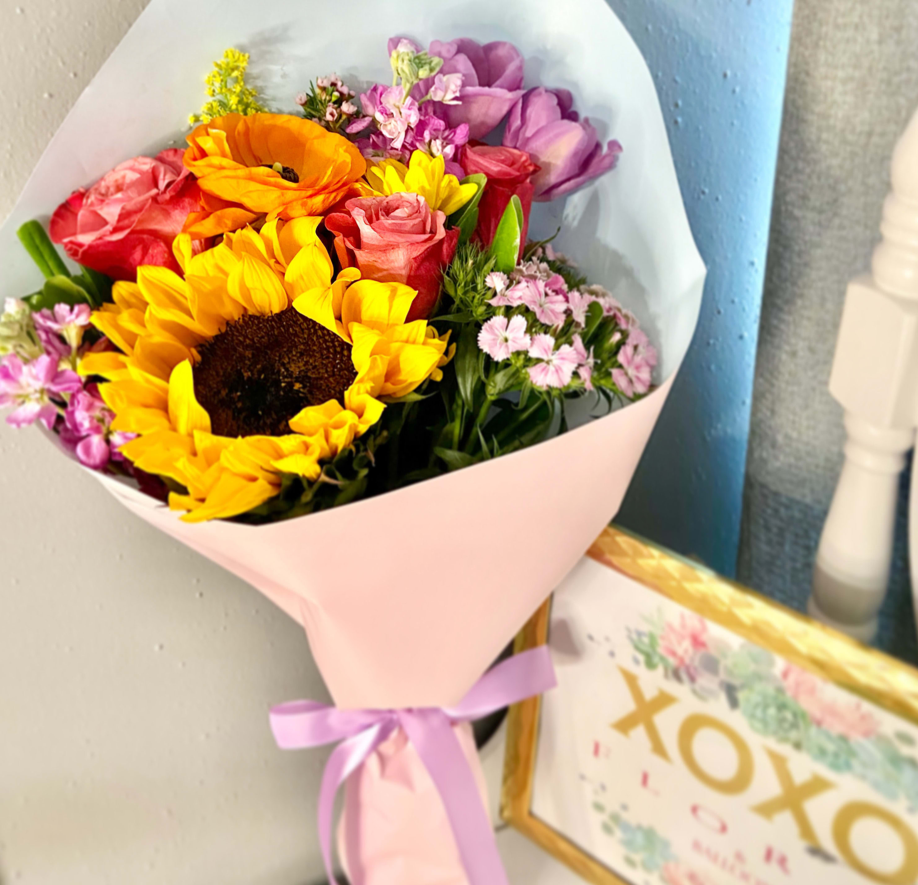 Bouquet of sunflowers, roses, and purple flowers wrapped in pink paper