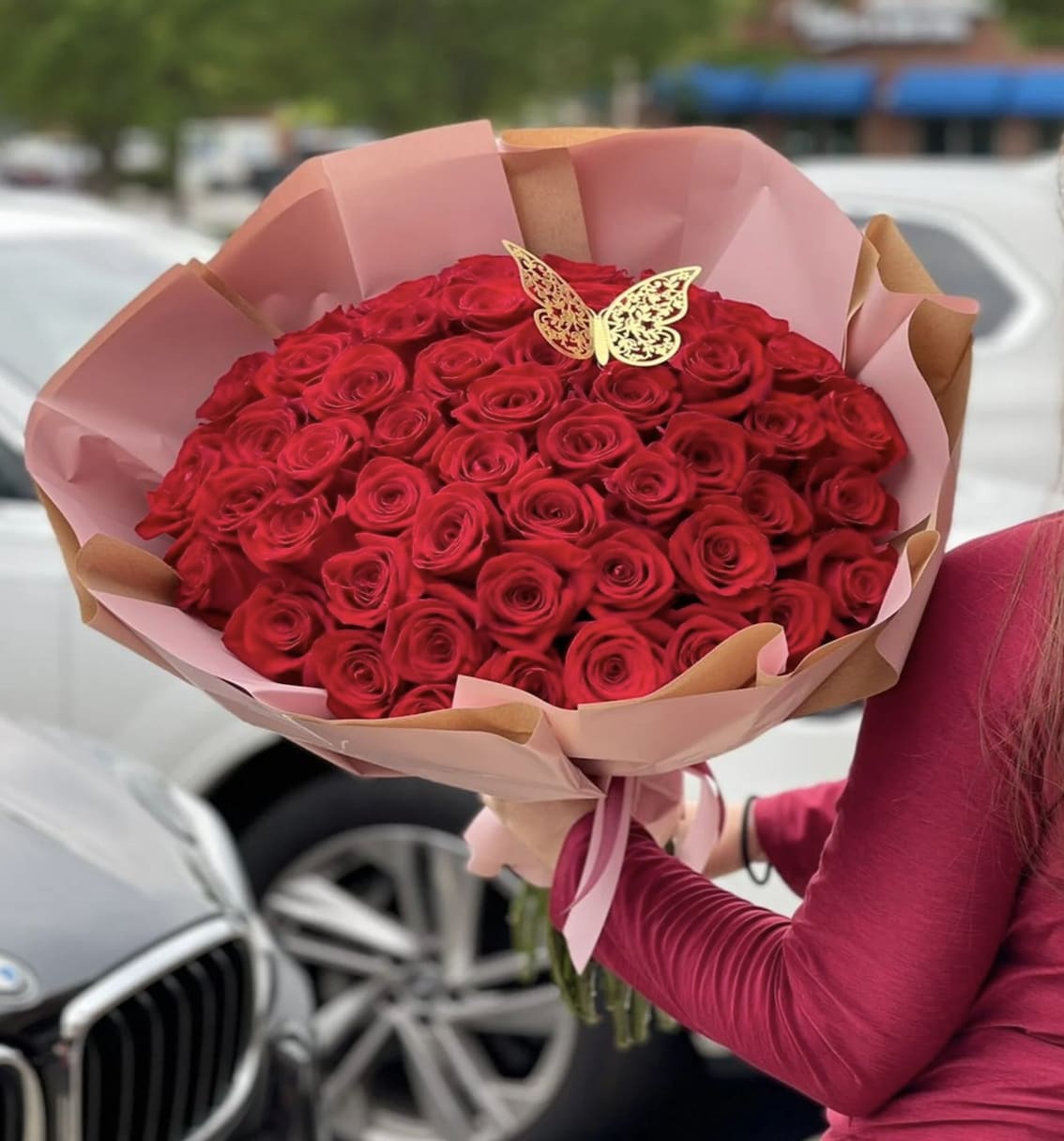 Large bouquet of red roses wrapped in pink paper with a butterfly topper