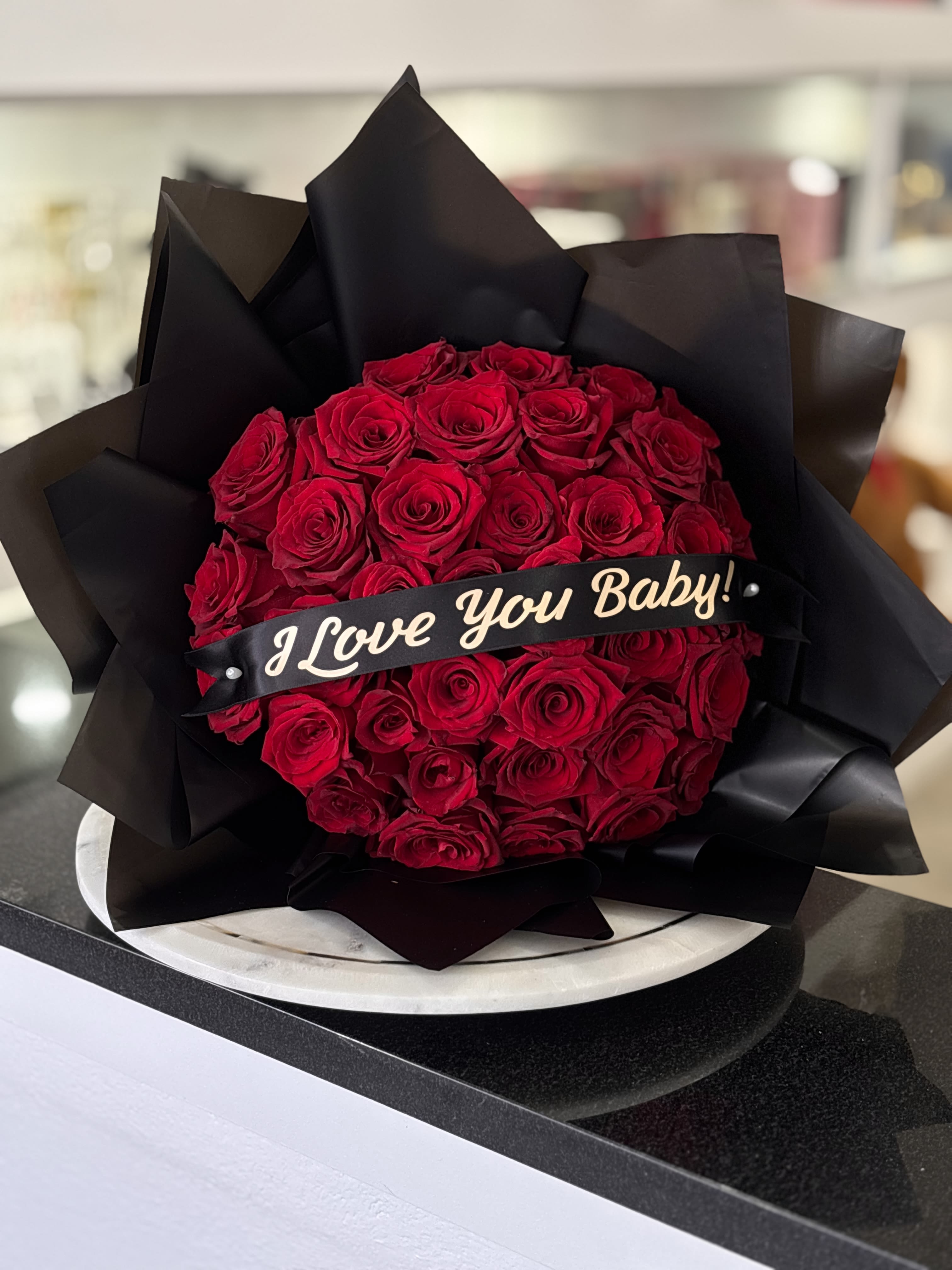Bouquet of red roses wrapped in black paper with a "I Love You Baby!" ribbon