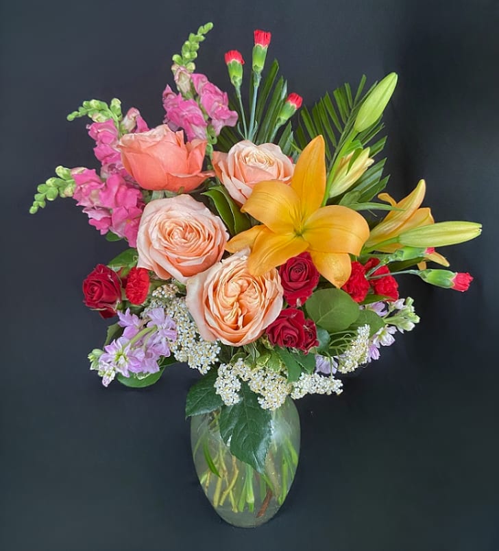 Mixed bouquet of roses, lilies, and snapdragons in a glass vase