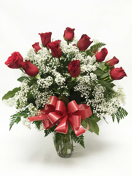 Dozen red roses with white filler flowers in a glass vase with a red ribbon bow