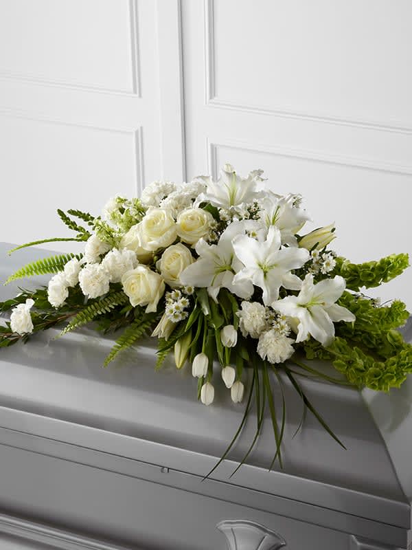 White roses, lilies, and tulips arranged in a long spray on top of a gray casket