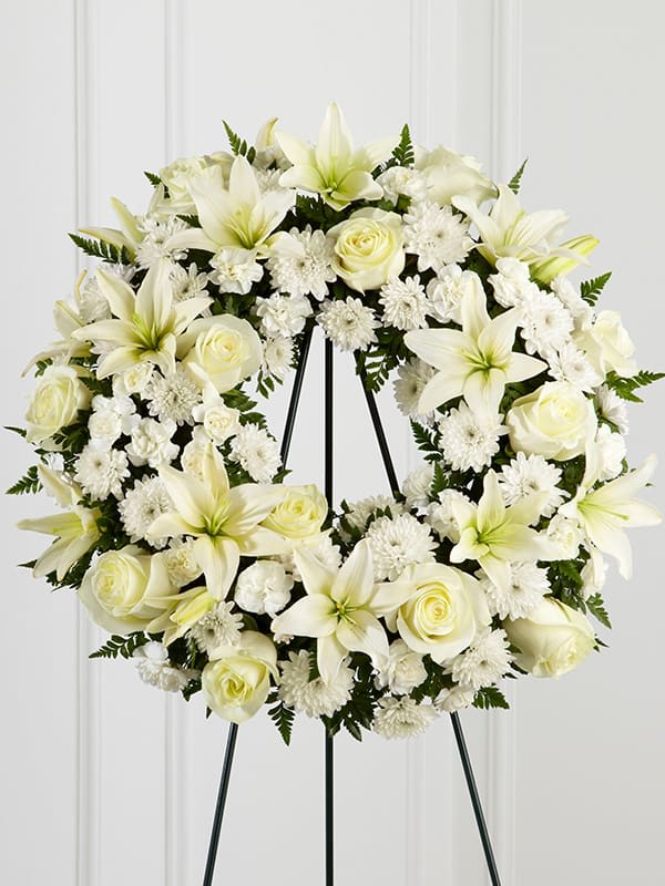 White wreath of lilies, roses, and chrysanthemums on a metal easel stand