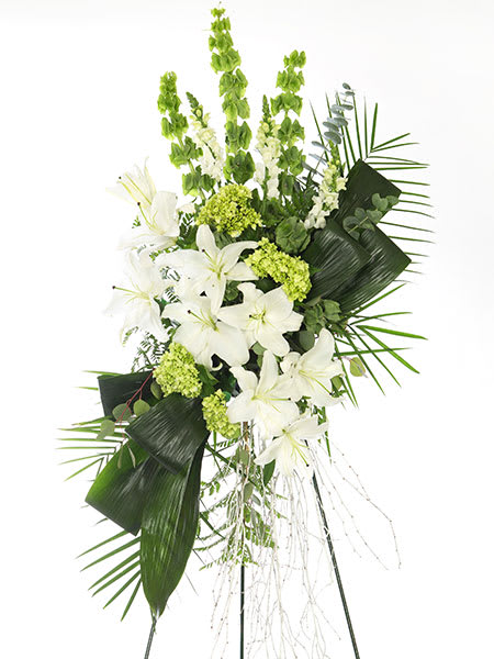 Tall white and green standing spray with lilies, snapdragons, and bold tropical leaves on a metal easel.