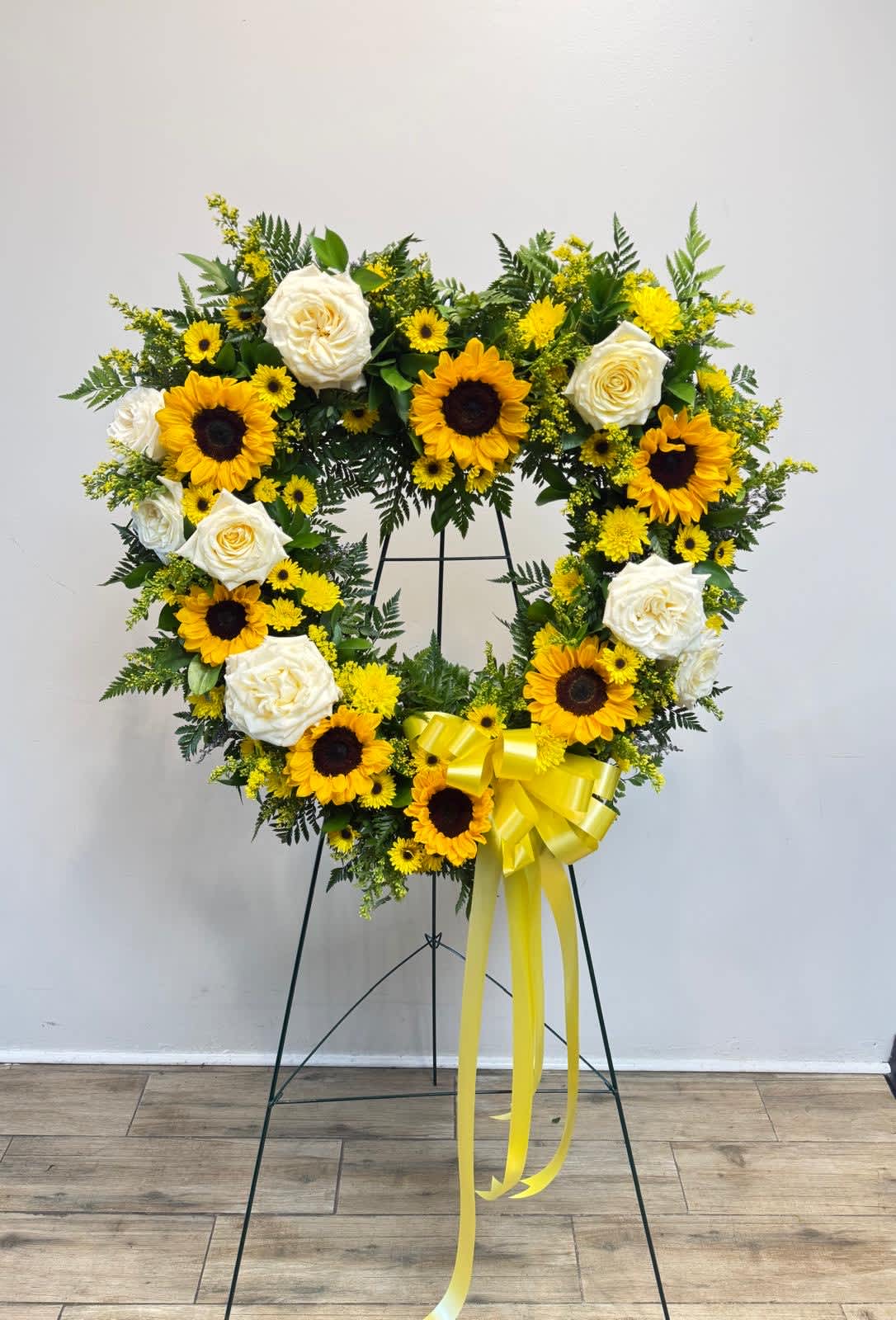 Heart-shaped floral wreath with sunflowers and white roses on a stand