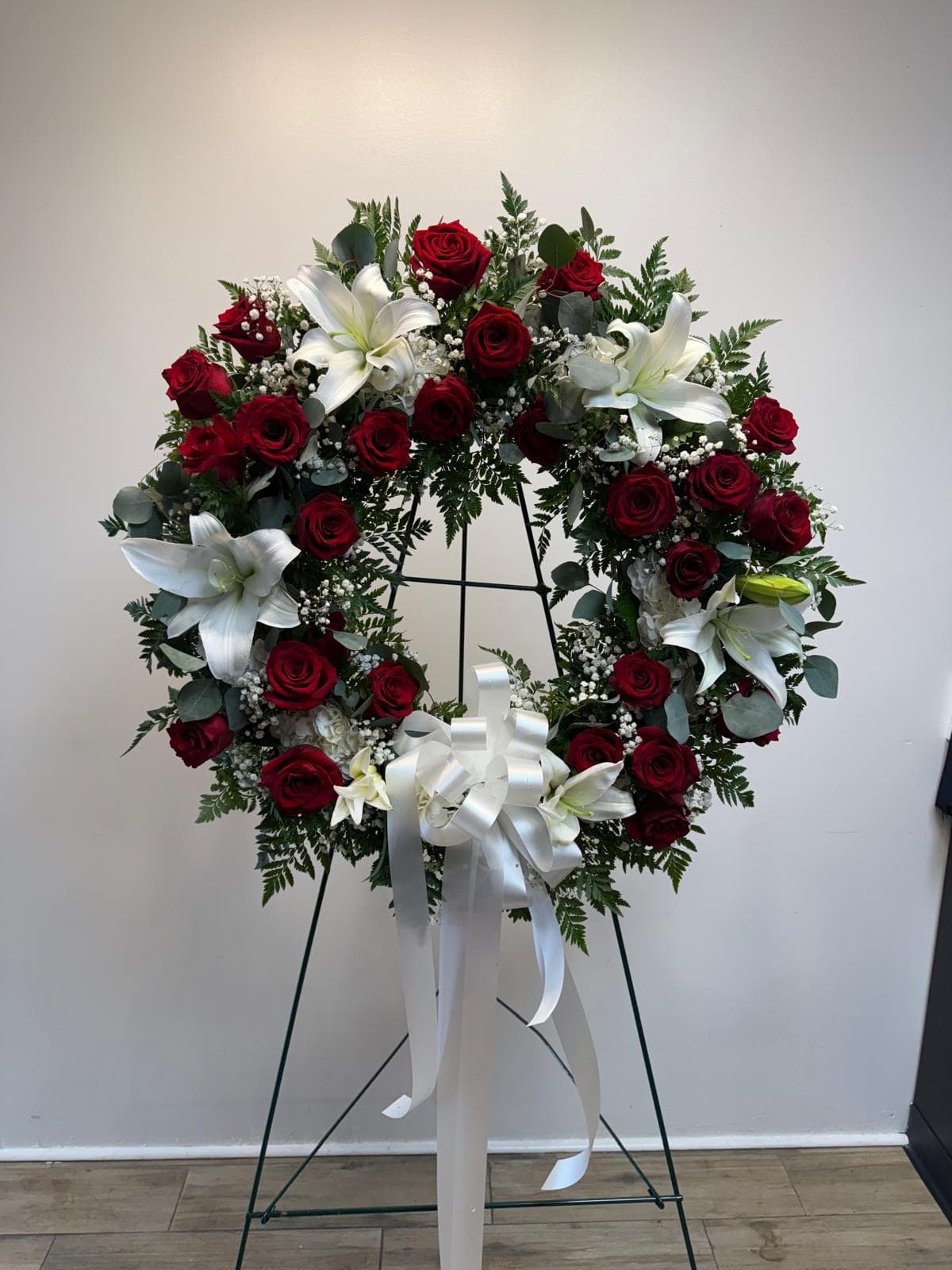 Circular wreath of red roses and white lilies on a stand with a white ribbon