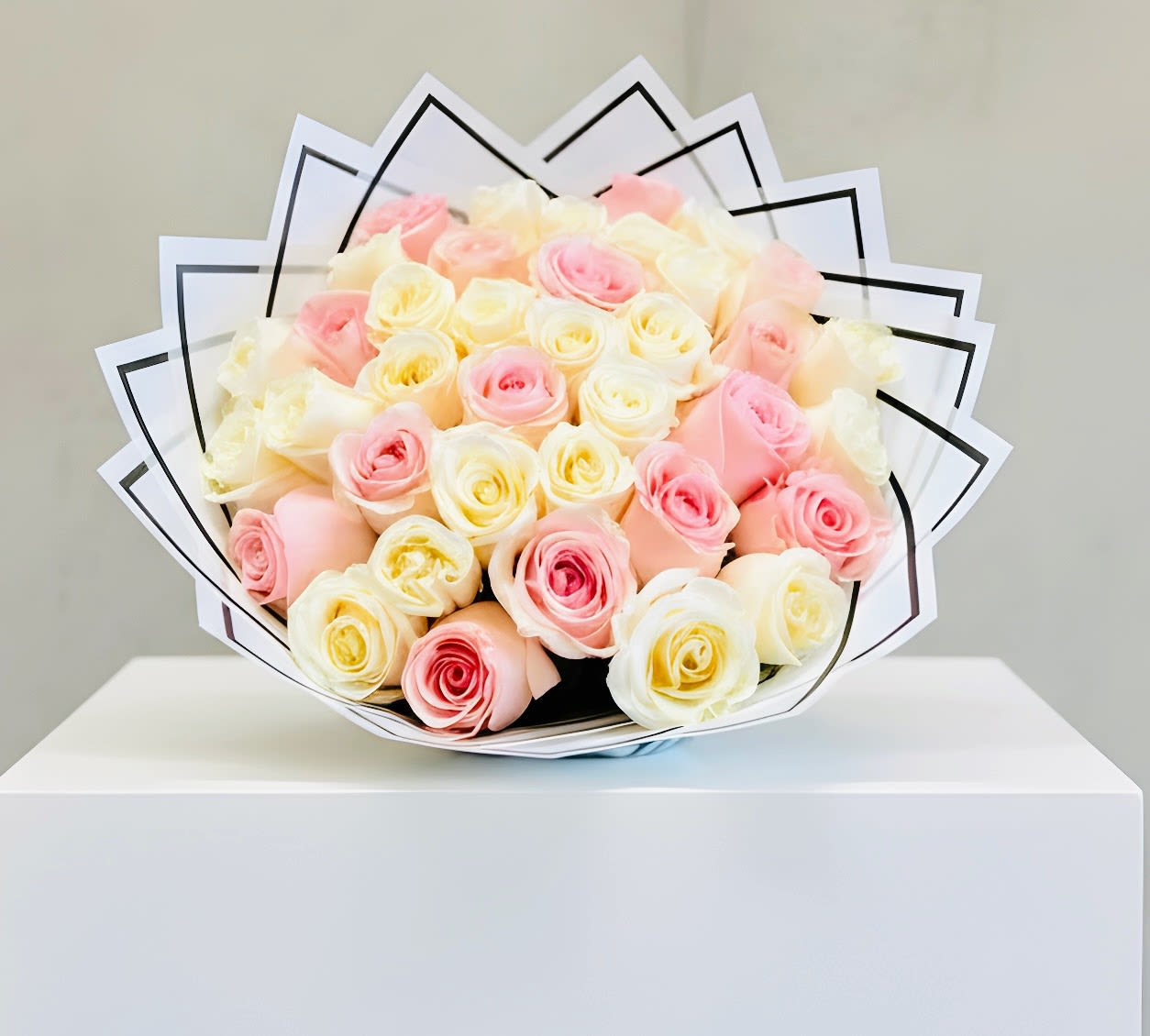 Round bouquet of cream and soft pink roses wrapped in layered white paper with black trim
