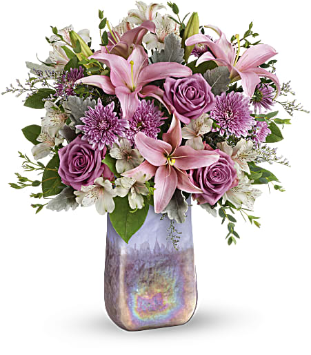 Pink lilies and lavender roses with white blooms in a tall iridescent vase