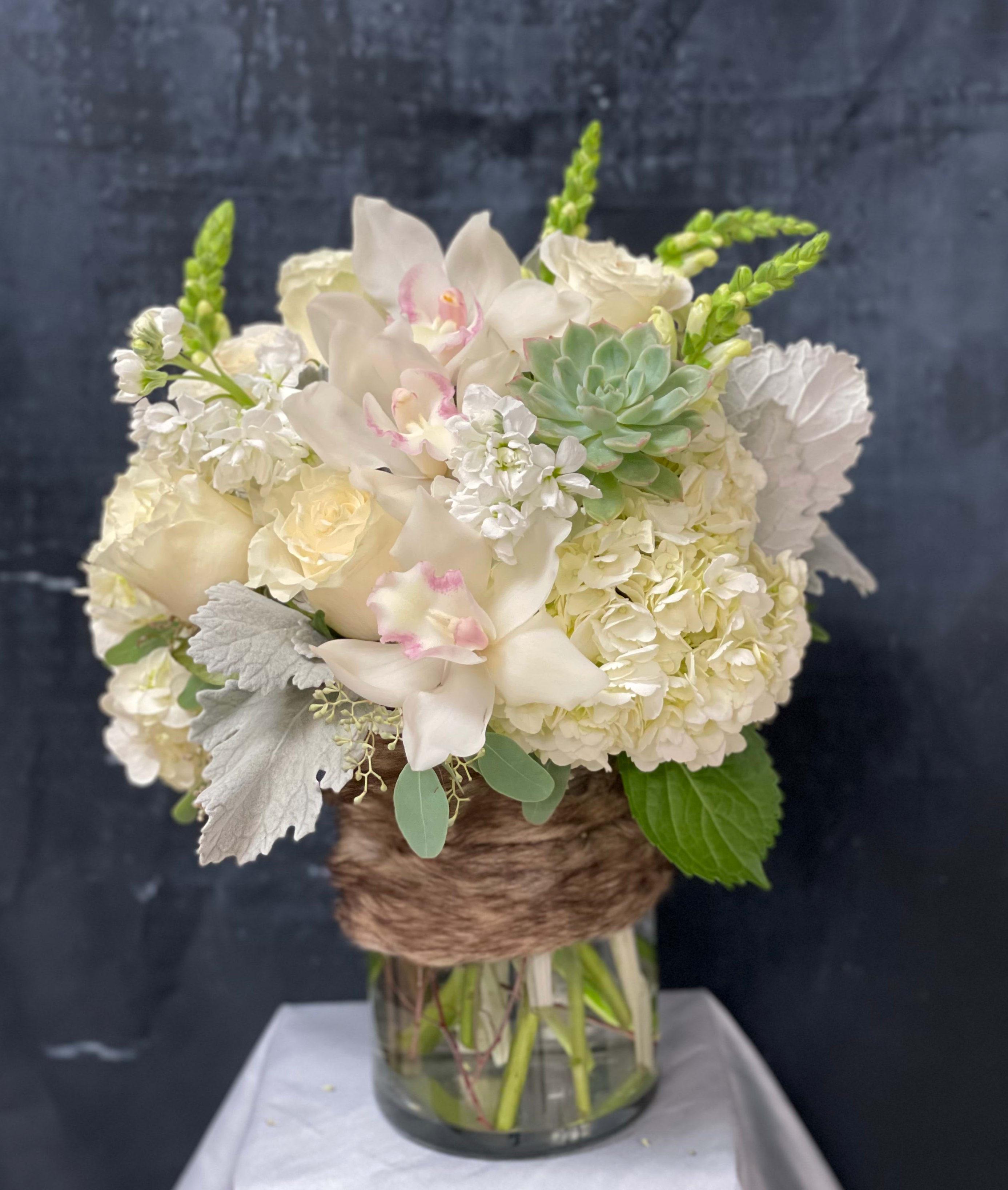 White hydrangeas, roses, orchids, and a succulent in a glass vase wrapped with brown twine