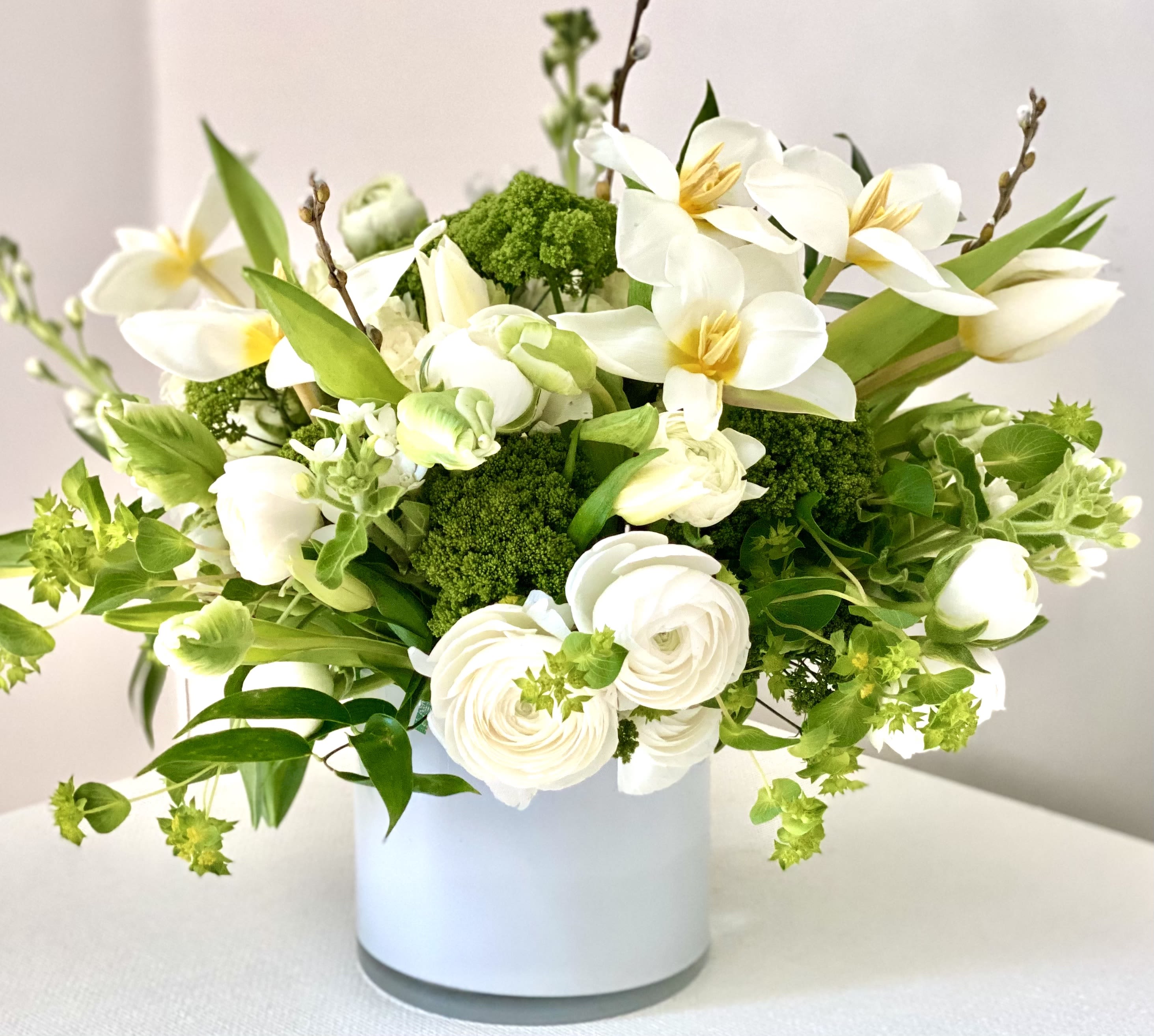 Clean whites + brights- Spring edition! - Gorgeous clean whites &amp; greens make this neutral palette a spring crowd pleaser.  We use gorgeous white tulips (when available), ranunculus &amp; sweet stock and add in greens both flowers and foliages like trick, green hydrangea and/or green tulips or hellebores.  This arrangement comes in a white glass vase is just a stunner.    Standard size comes in a 5x5 white glass or ceramic vessel Deluxe is a 6x6 size white glass vessel Premium comes in a taller vase white ceramic approx 10" x 4-5"  We will sub in clear glass lined with green leaf as needed.   This is wonderful for so many occassions and a very nice expression for sympathy. 