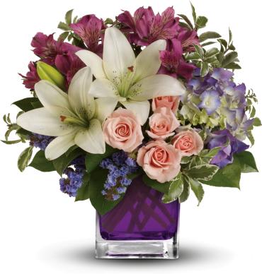 Bouquet of white lilies, pink roses, and purple flowers in a purple glass vase