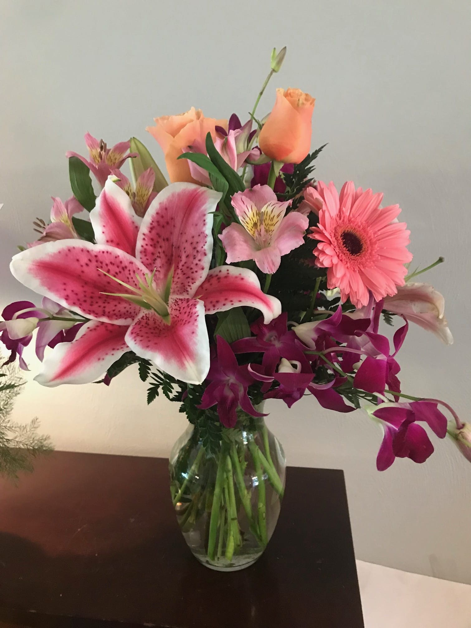 Mixed bouquet of pink lilies, roses, and a gerbera daisy in a glass vase