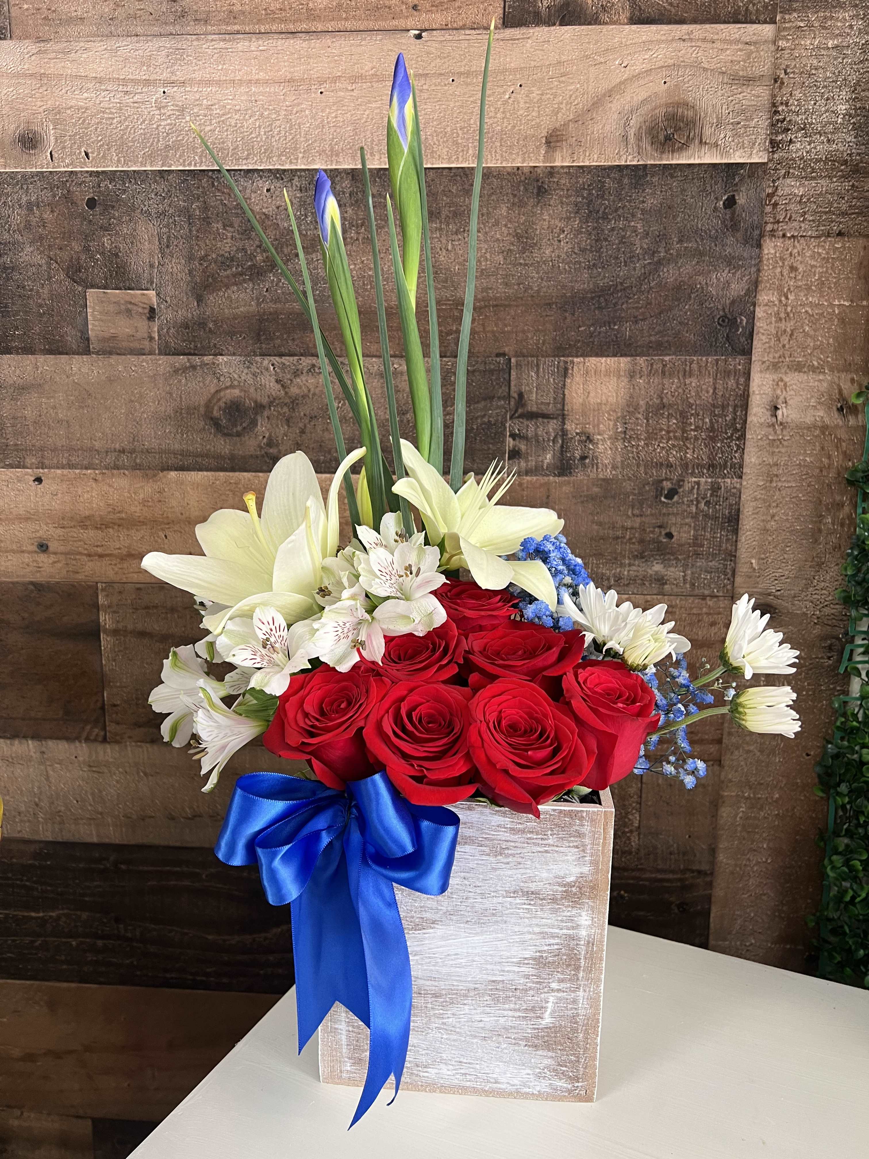 Red roses and white lilies in a wooden box with a blue ribbon