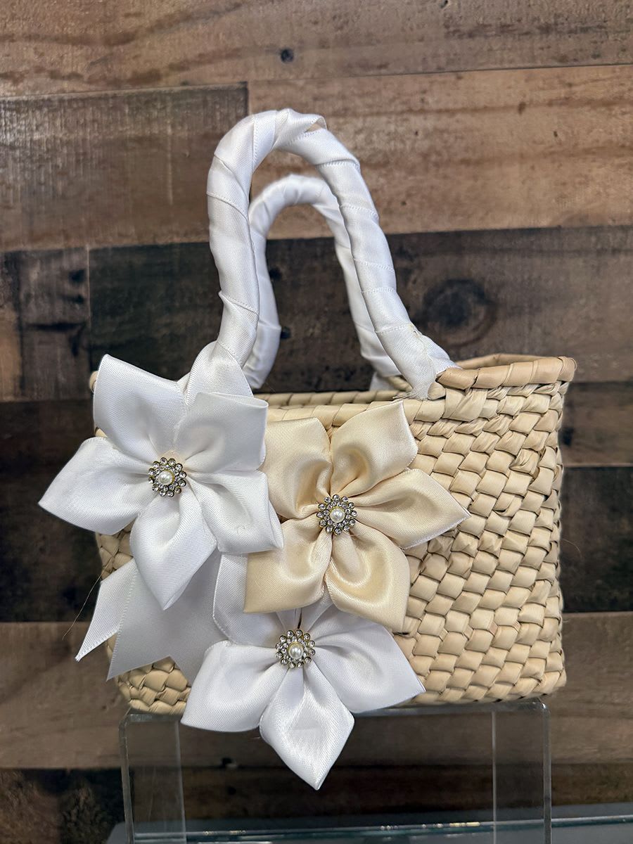 Artisan Purse - White Theme - A handcrafted woven straw handbag trimmed with satin ribbon flowers and sparkling rhinestone centers makes a charming gift-ready accessory for a spring baby shower, birthday, or hostess present. This small woven basket-style arrangement reads like a polished keepsake rather than a traditional bouquet-its bright blue and pale blue satin blooms (with jeweled centers) or the softer ivory, champagne and gold ribbon flowers bring instant cheer and a touch of couture to the recipient's moment.  Each handbag features natural straw texture, two wrapped handles, and decorative satin ribbon flowers finished with rhinestone brooch centers for a playful yet elegant look. Sizes are compact and structured-perfect for pairing with small gifts, note cards, or a single posy if the recipient prefers-even when no fresh flowers are included the piece feels celebratory. Choose the colorway that suits the occasion: bold red flowers for a festive pop, bright blue for a spring or baby-themed surprise, or neutral champagne and ivory for a more formal gift.