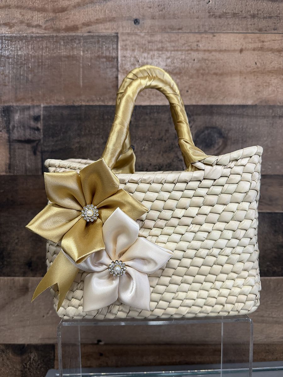 Artisan Purse - Gold Theme - A handcrafted woven straw handbag trimmed with satin ribbon flowers and sparkling rhinestone centers makes a charming gift-ready accessory for a spring baby shower, birthday, or hostess present. This small woven basket-style arrangement reads like a polished keepsake rather than a traditional bouquet-its bright blue and pale blue satin blooms (with jeweled centers) or the softer ivory, champagne and gold ribbon flowers bring instant cheer and a touch of couture to the recipient's moment.  Each handbag features natural straw texture, two wrapped handles, and decorative satin ribbon flowers finished with rhinestone brooch centers for a playful yet elegant look. Sizes are compact and structured-perfect for pairing with small gifts, note cards, or a single posy if the recipient prefers-even when no fresh flowers are included the piece feels celebratory. Choose the colorway that suits the occasion: bold red flowers for a festive pop, bright blue for a spring or baby-themed surprise, or neutral champagne and ivory for a more formal gift.