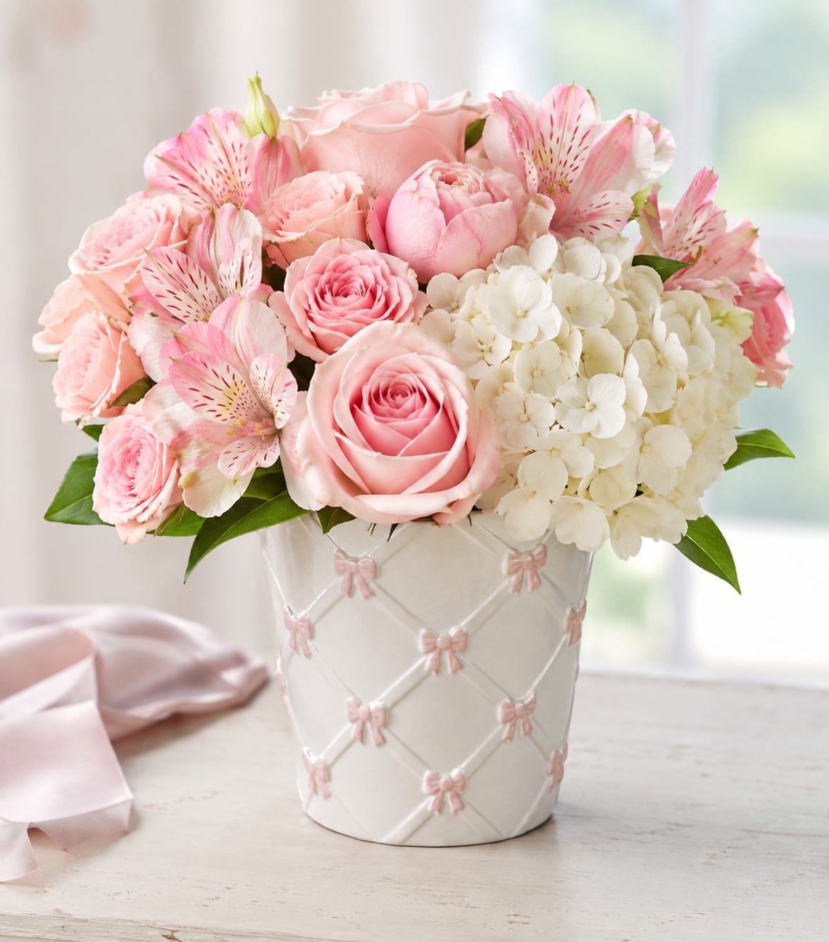 Pink roses and alstroemeria arranged in a white vase with pink bows