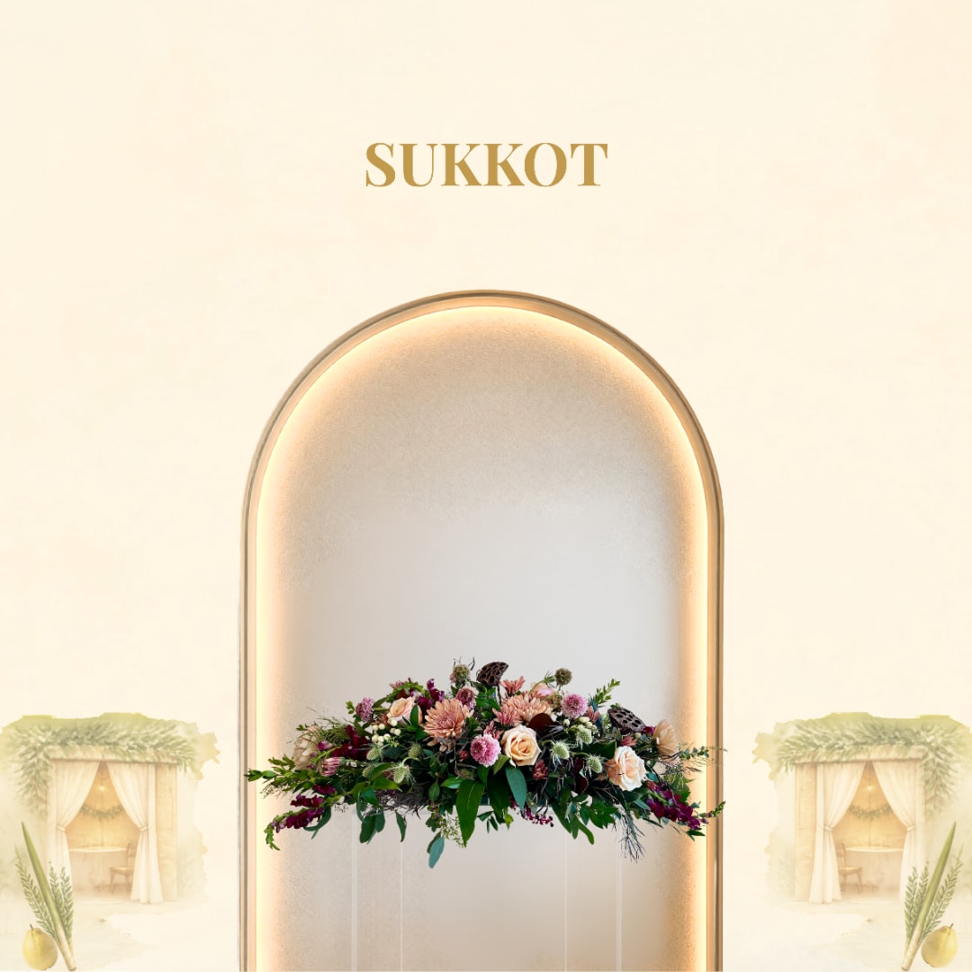 Low floral centerpiece with pink and peach blooms under the word Sukkot