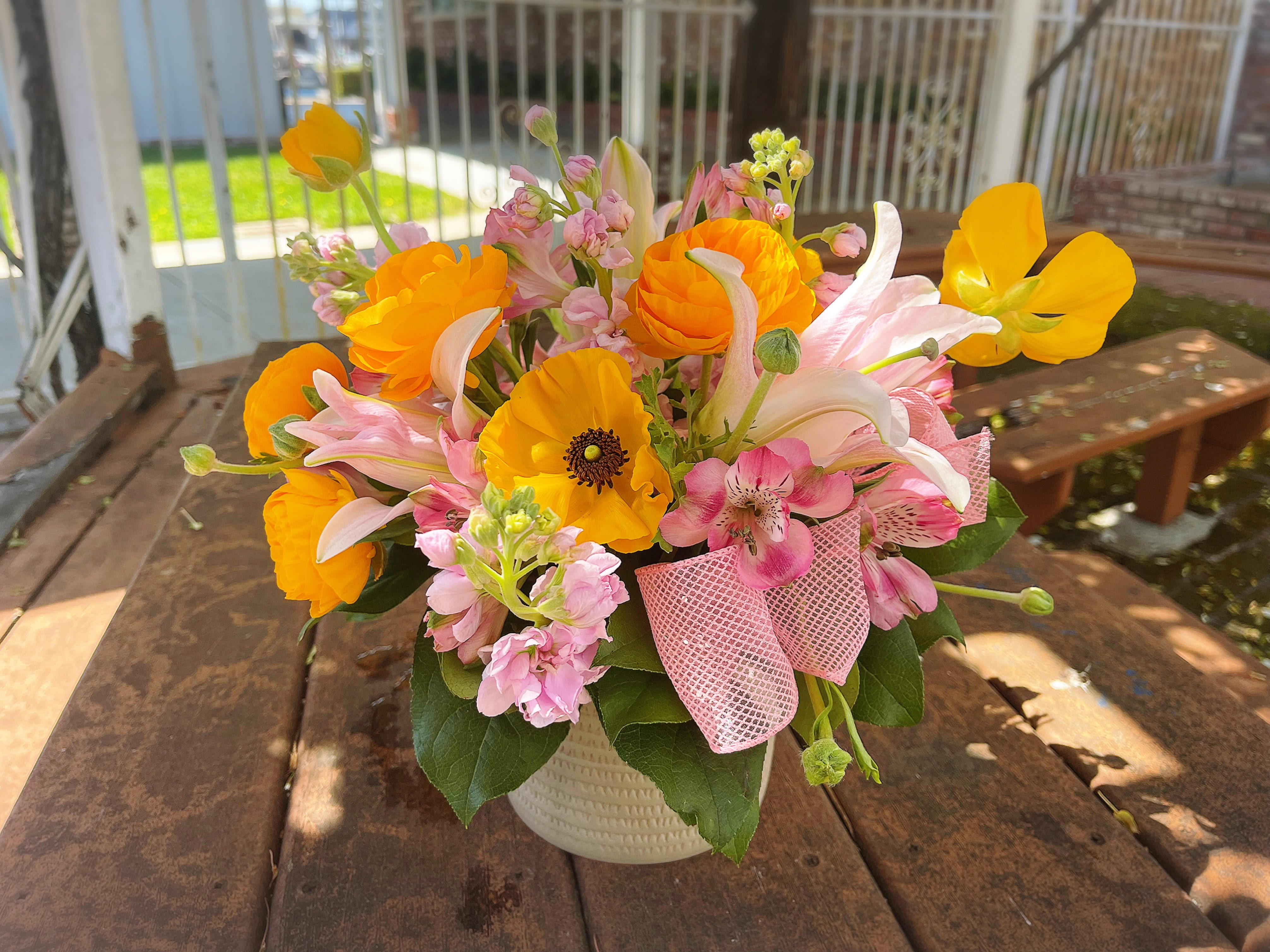 Bouquet of orange and pink flowers in a white vase with a pink ribbon