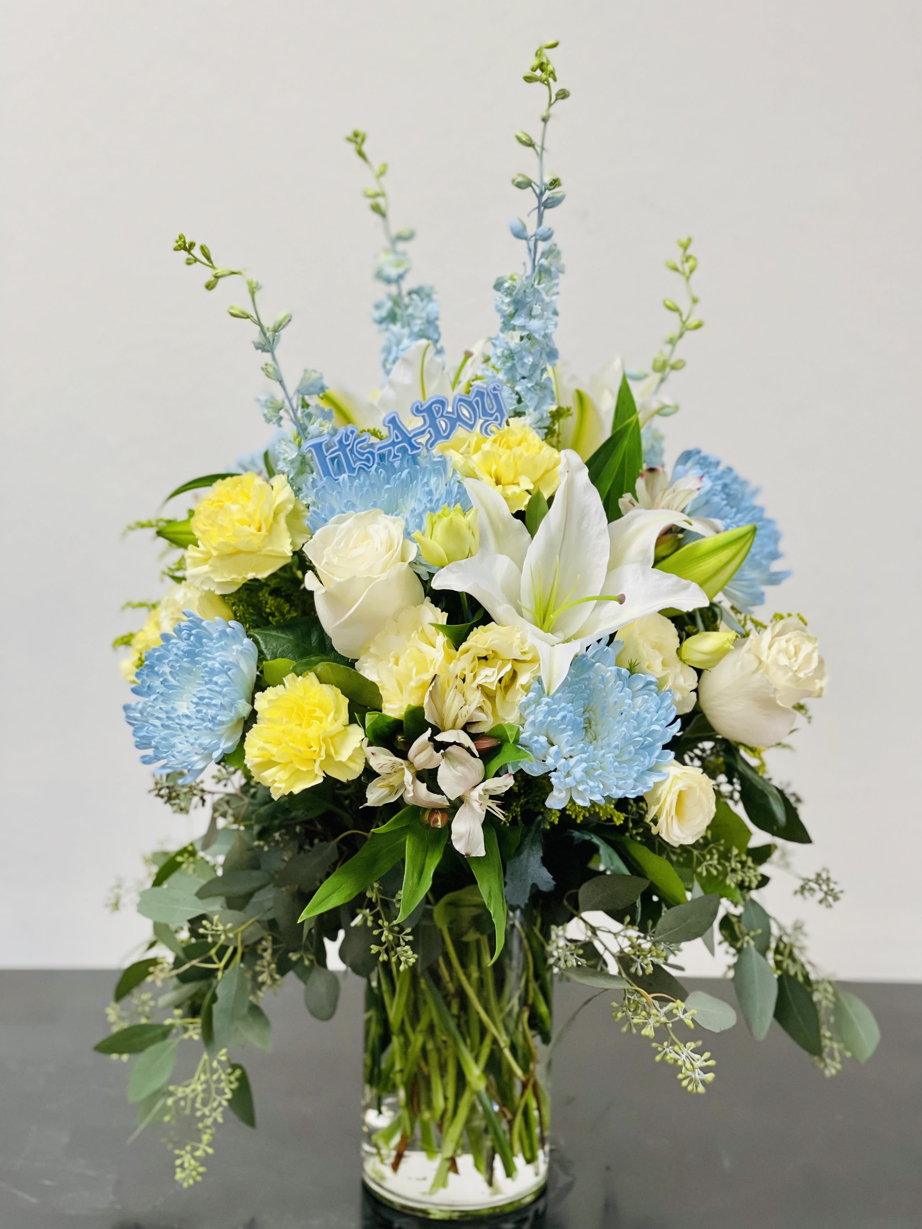 Blue and yellow floral arrangement in a glass vase with a "It's a Boy" topper