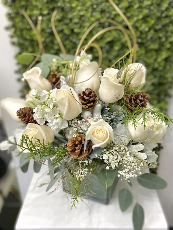 White rose arrangement with pinecones in a square vase against a green textured backdrop