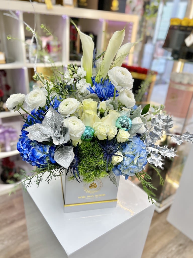 Box arrangement of white calla lilies, roses, and blue hydrangeas with silver accents in a white square container