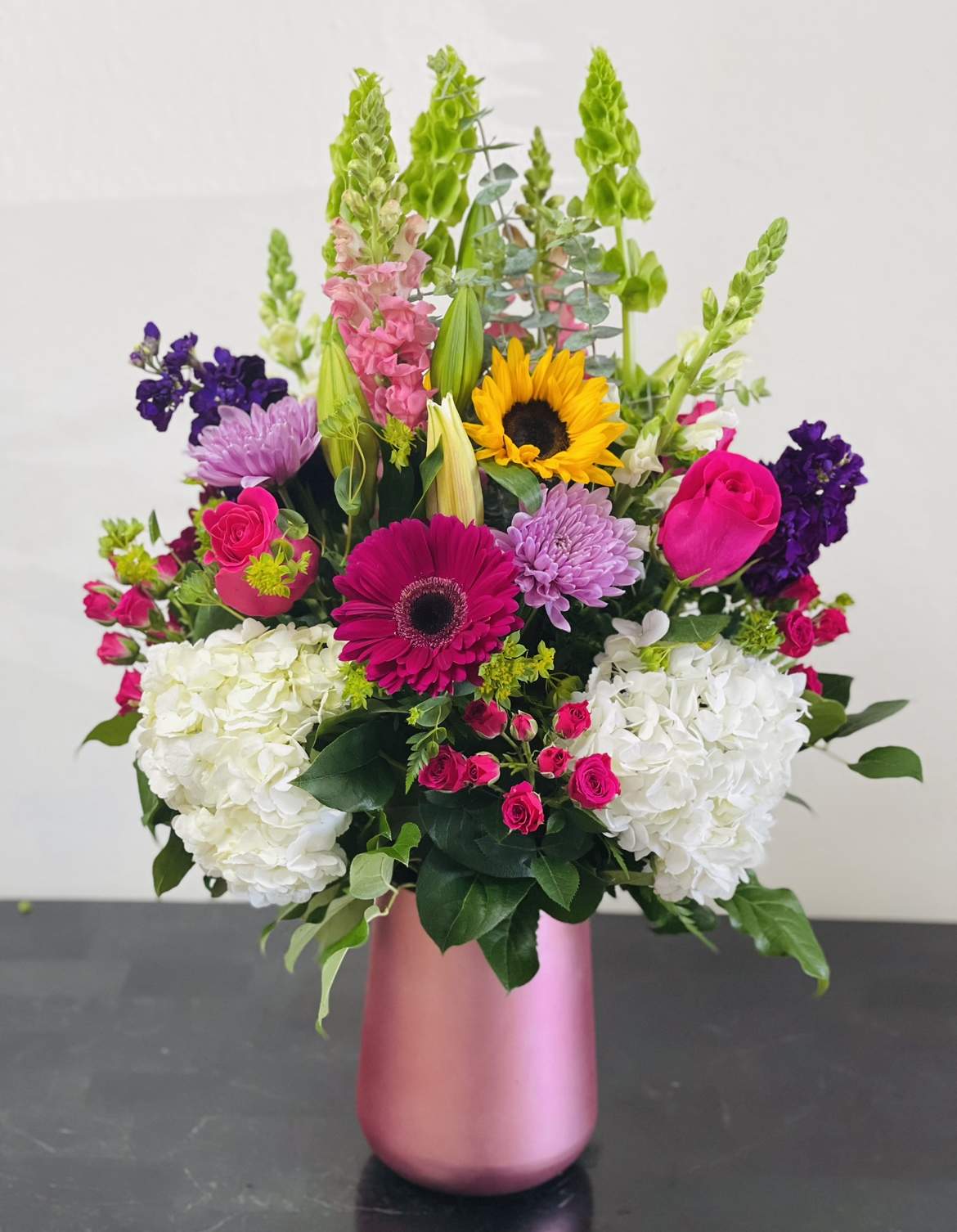 Mixed bouquet in a pink vase with sunflowers, roses, hydrangeas, and purple blooms