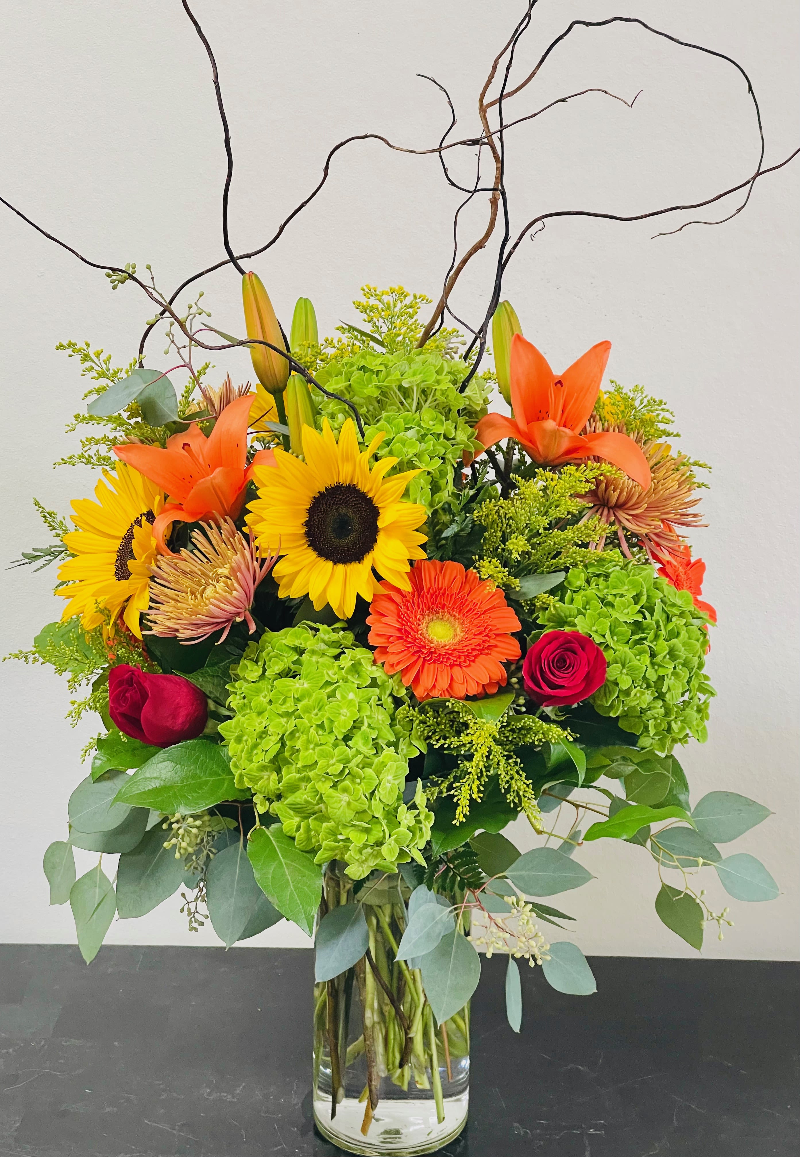 Bright mixed bouquet in a clear glass vase with sunflowers, lilies, and orange blooms