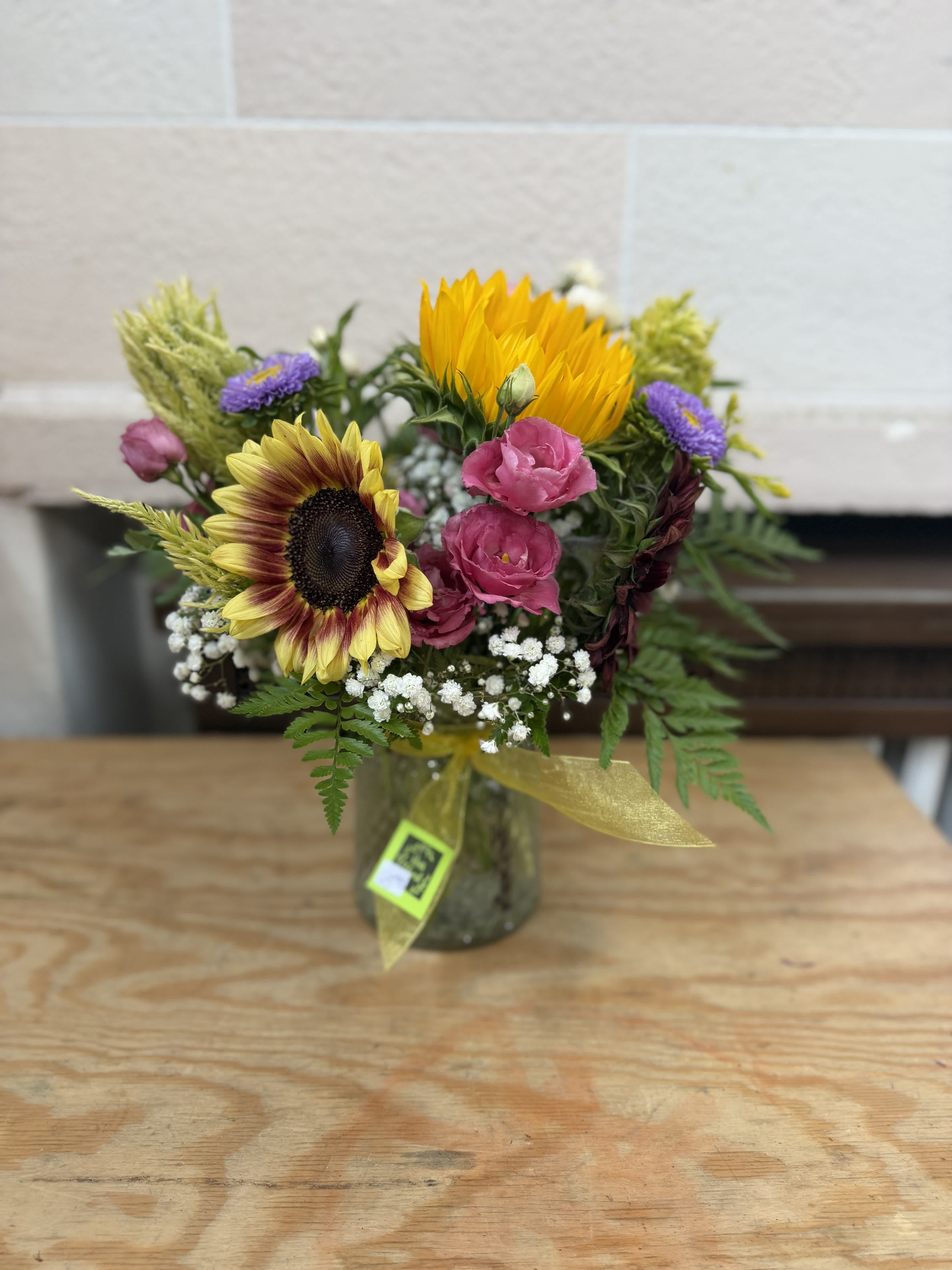 Mixed bouquet with sunflowers, pink blooms, and purple flowers in a glass jar