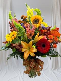 Colorful mixed bouquet with sunflowers, lilies, and gerbera daisies in a glass vase