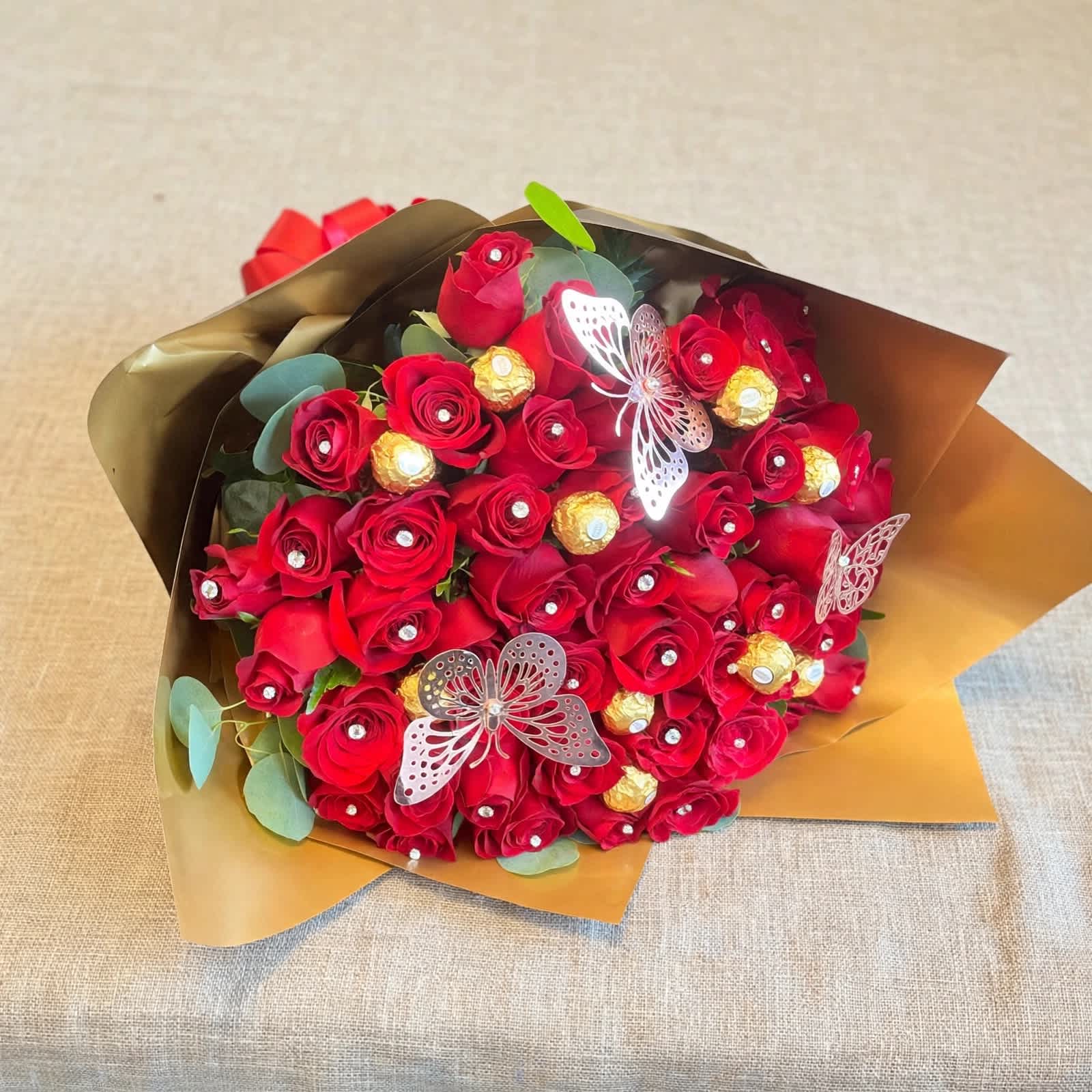Bouquet of red roses with gold-wrapped chocolates and butterfly accents