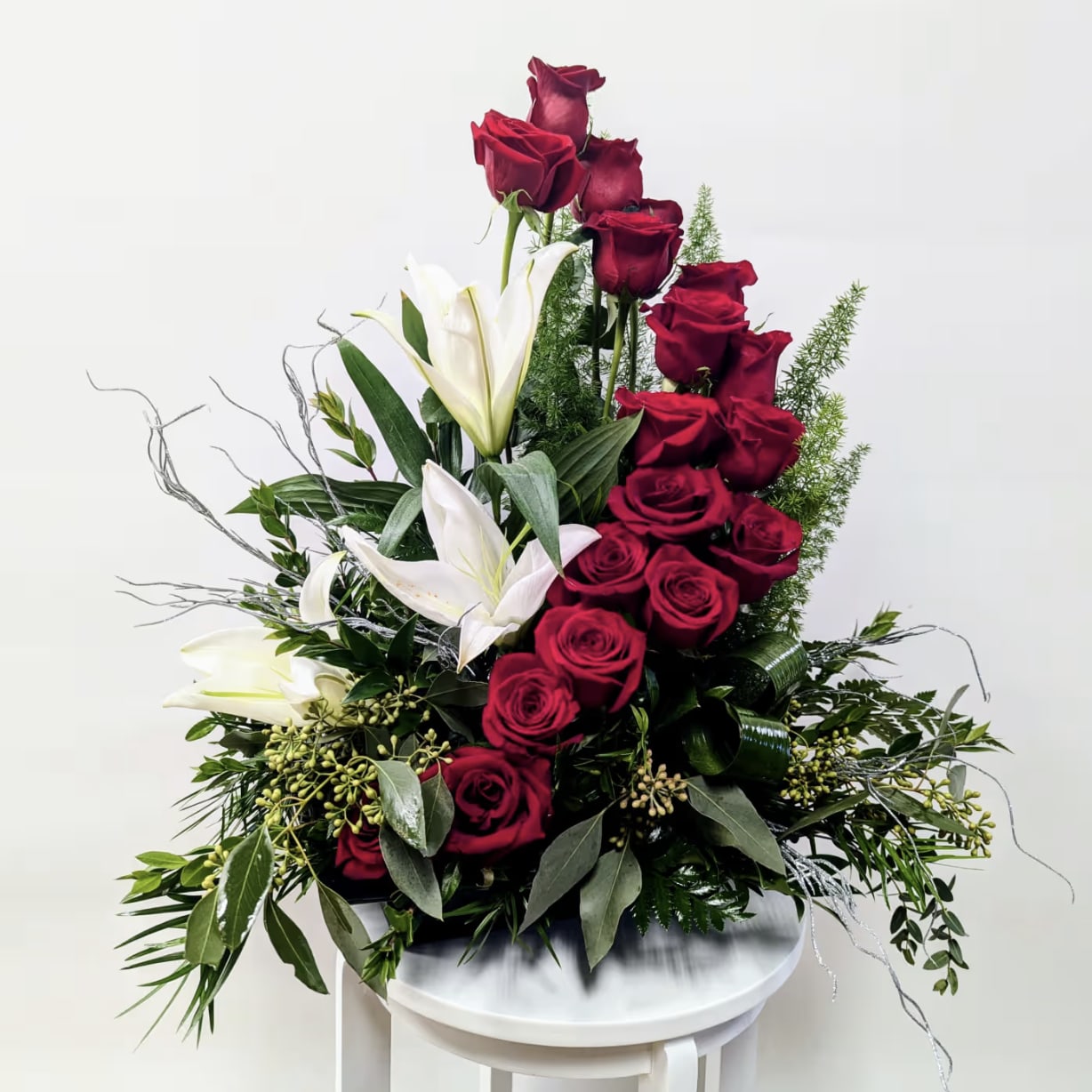 Elegance in Bloom - ake a bold and timeless statement with our Elegance in Bloom arrangement. This breathtaking display features a cascading design of deep red roses, symbolizing love and passion, paired beautifully with the grace of pure white lilies. Lush greenery and delicate decorative accents complete the look, making it a perfect choice for romantic gestures, sympathy tributes, or elegant celebrations.   Perfect for: Anniversaries, Sympathy, Romantic Occasions, and Grand Gestures Includes: Premium red roses, white lilies, fresh greenery, and artistic decorative touches. 