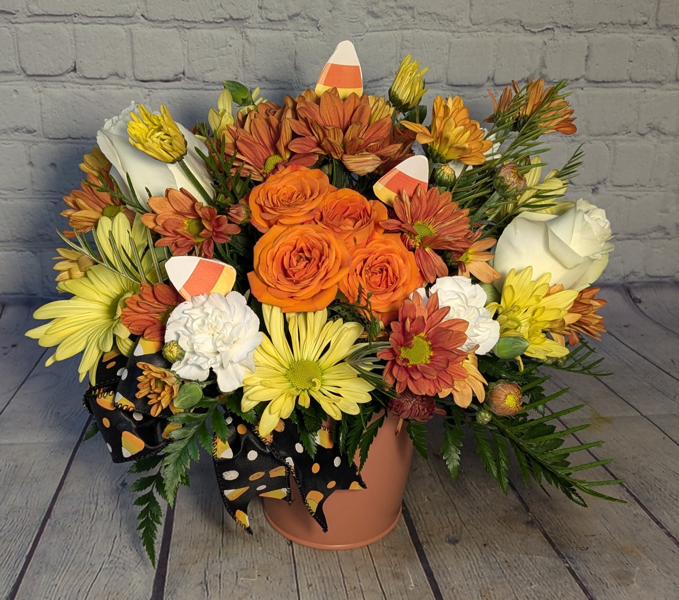 Orange and yellow flower arrangement in a peach vase with a black polka-dot ribbon