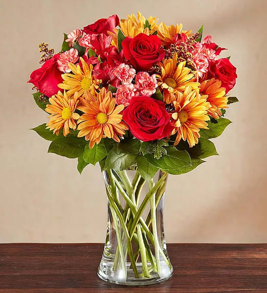 Bouquet of red roses and yellow daisies in a clear glass vase
