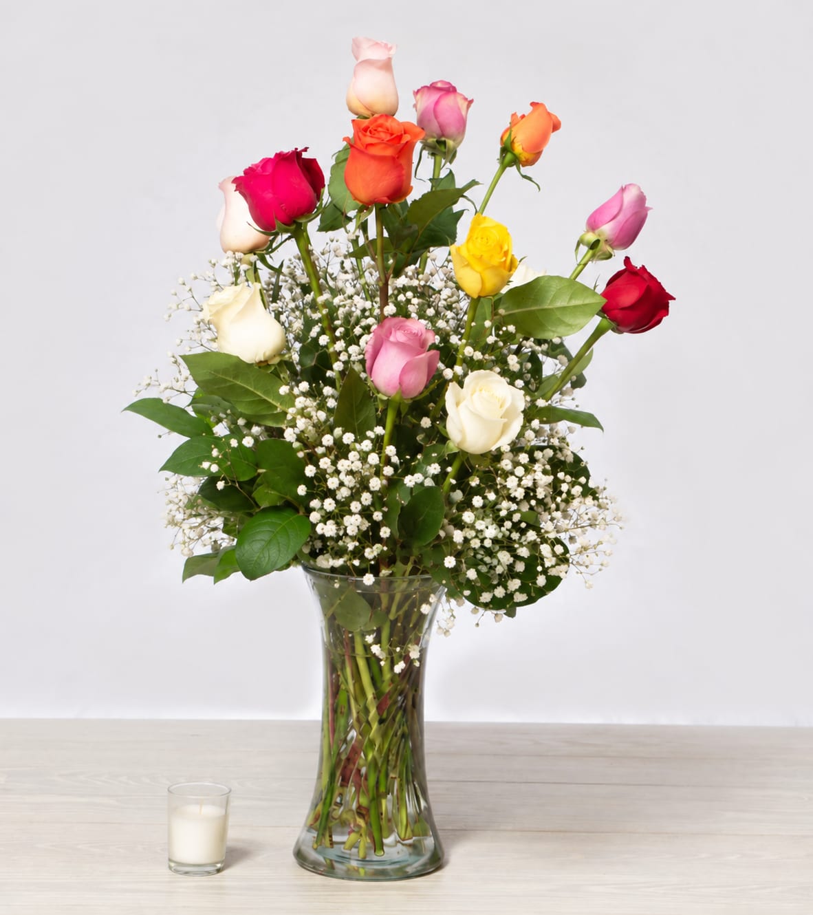 Mixed roses in a clear glass vase with baby's breath and a candle nearby