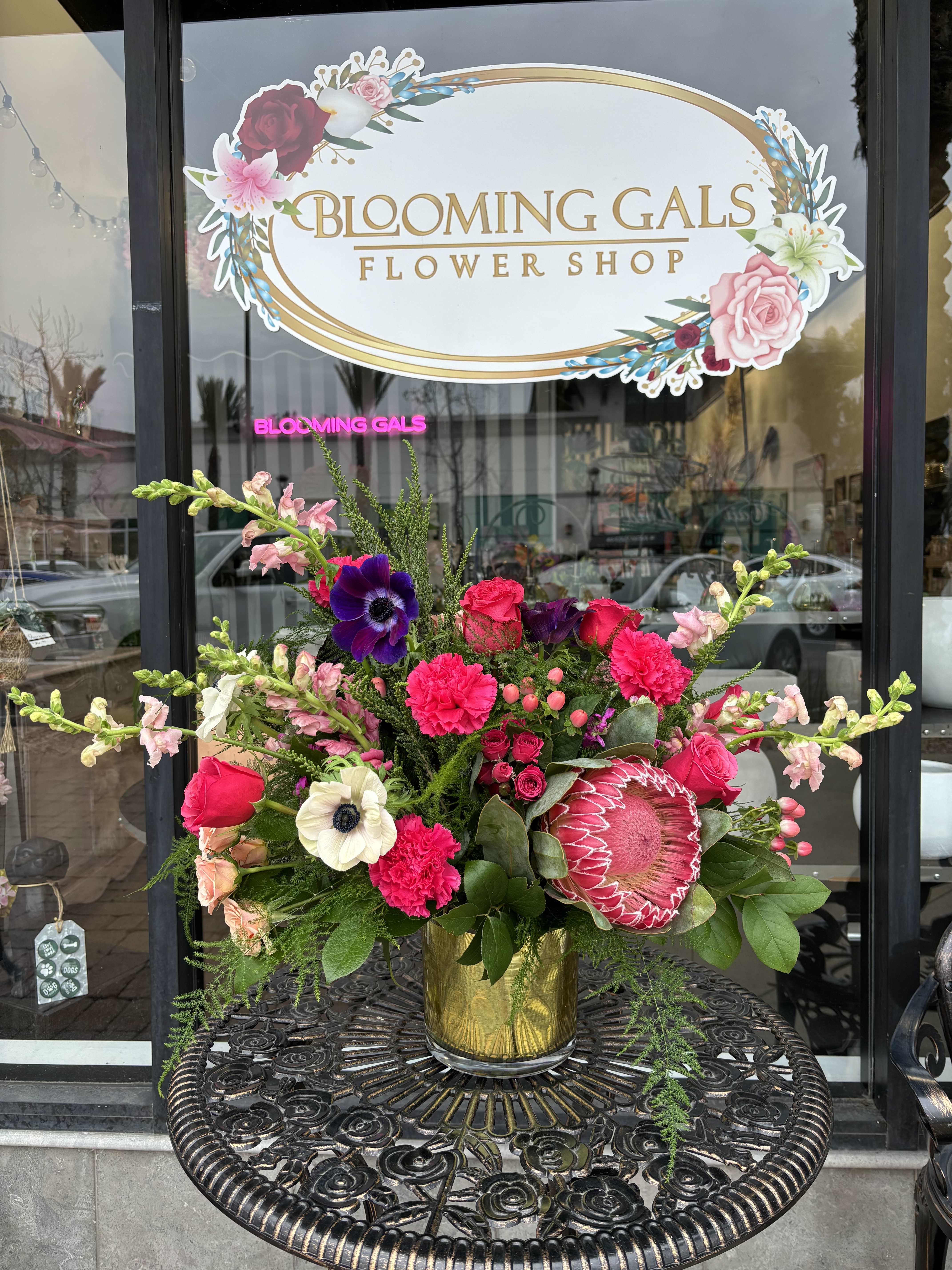 Bright mixed flower arrangement in a gold vase on a metal table