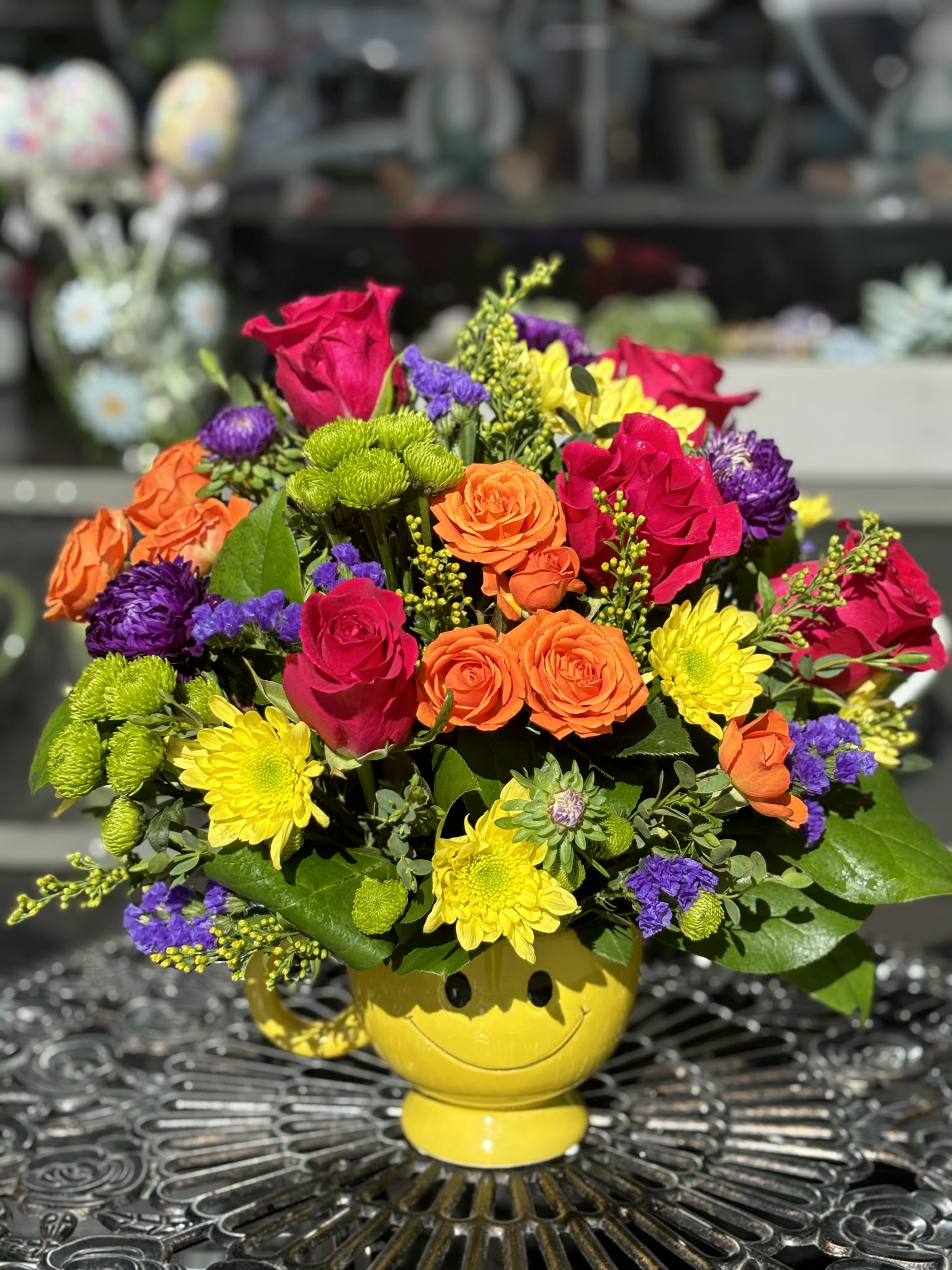 Mixed bouquet in a yellow smiley-face vase with roses and mums