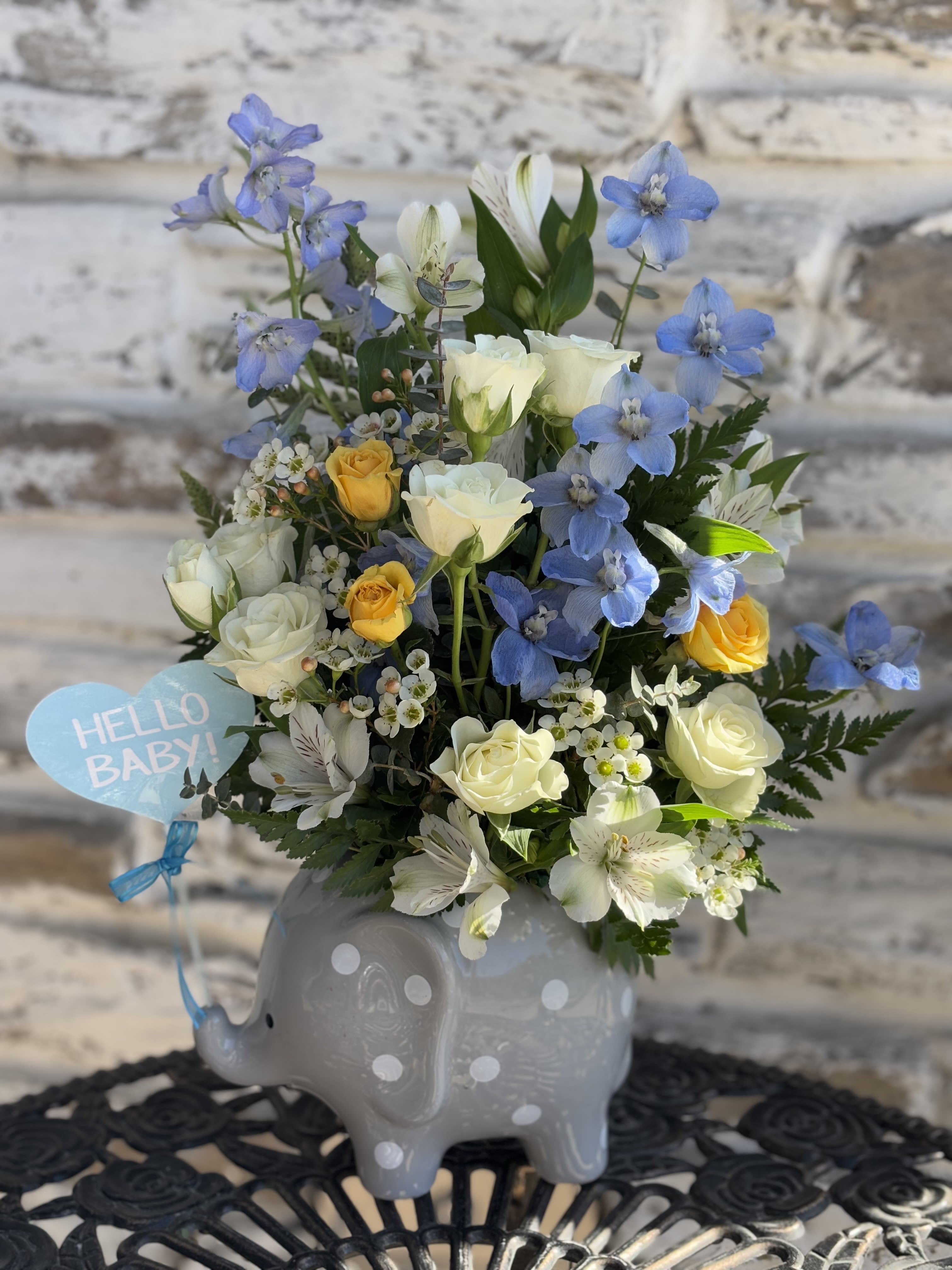 Blue and white flower arrangement in a gray elephant vase with a "Hello Baby" tag