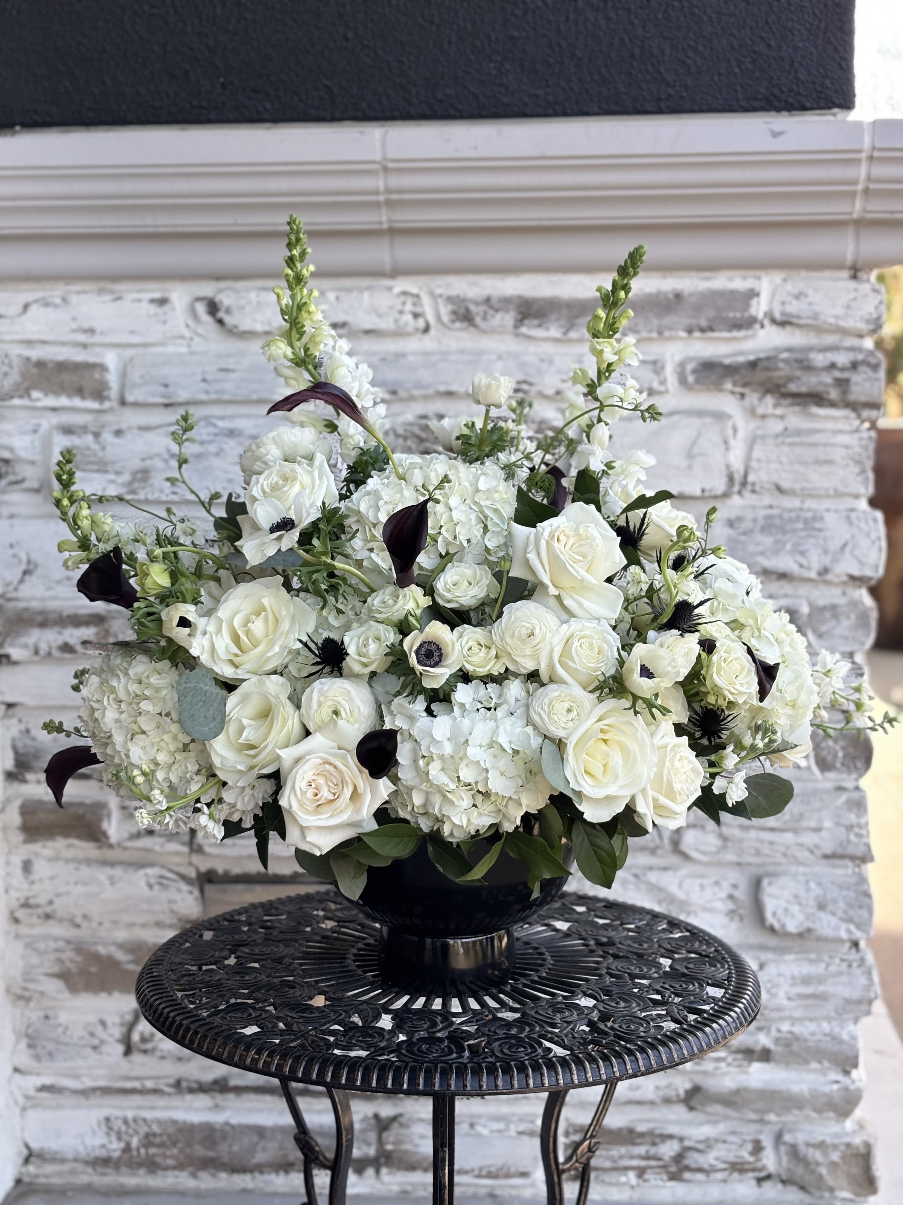 White floral arrangement in a black vase with dark accent blooms