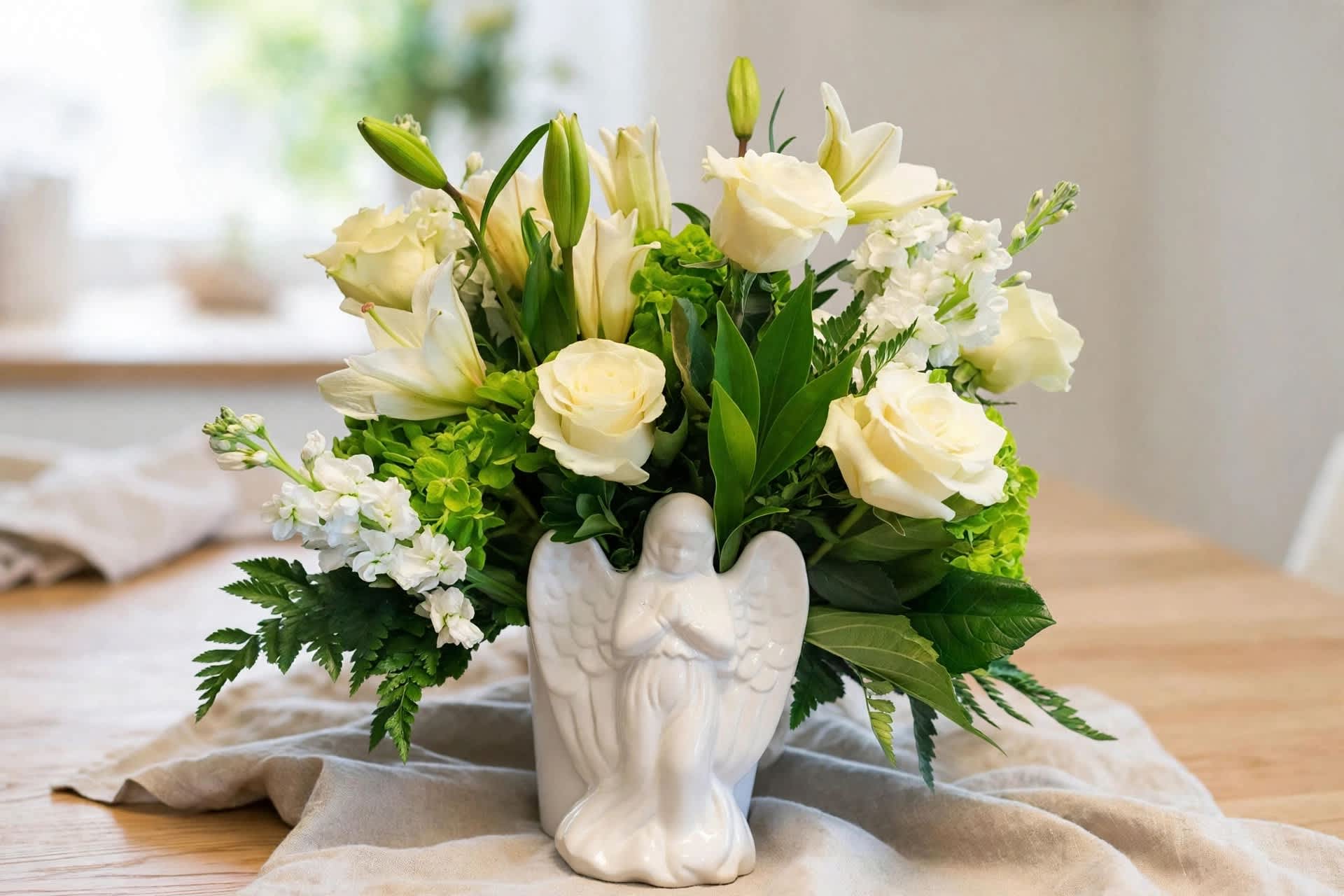 White roses and lilies arranged in a white angel vase