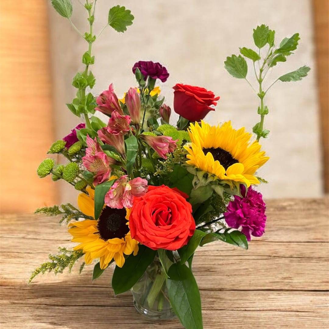 Mixed bouquet with sunflowers, red roses, and pink alstroemeria in a glass vase