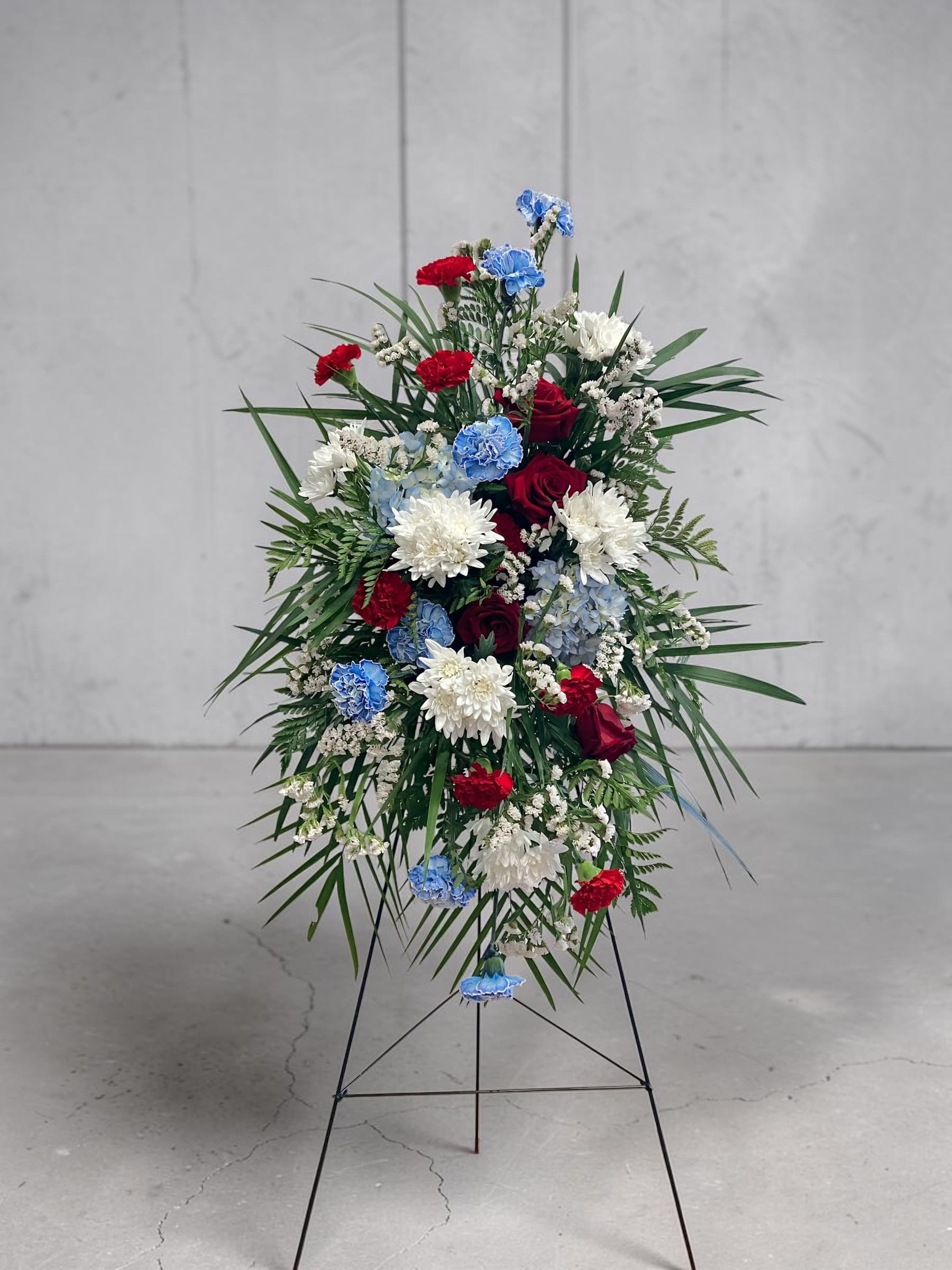 Standing floral spray with red, white, and blue flowers on a metal easel
