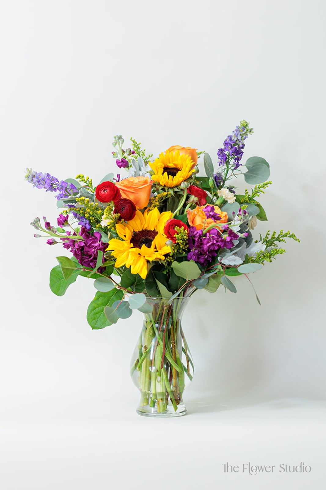Mixed bouquet of sunflowers, roses, and purple flowers in a glass vase