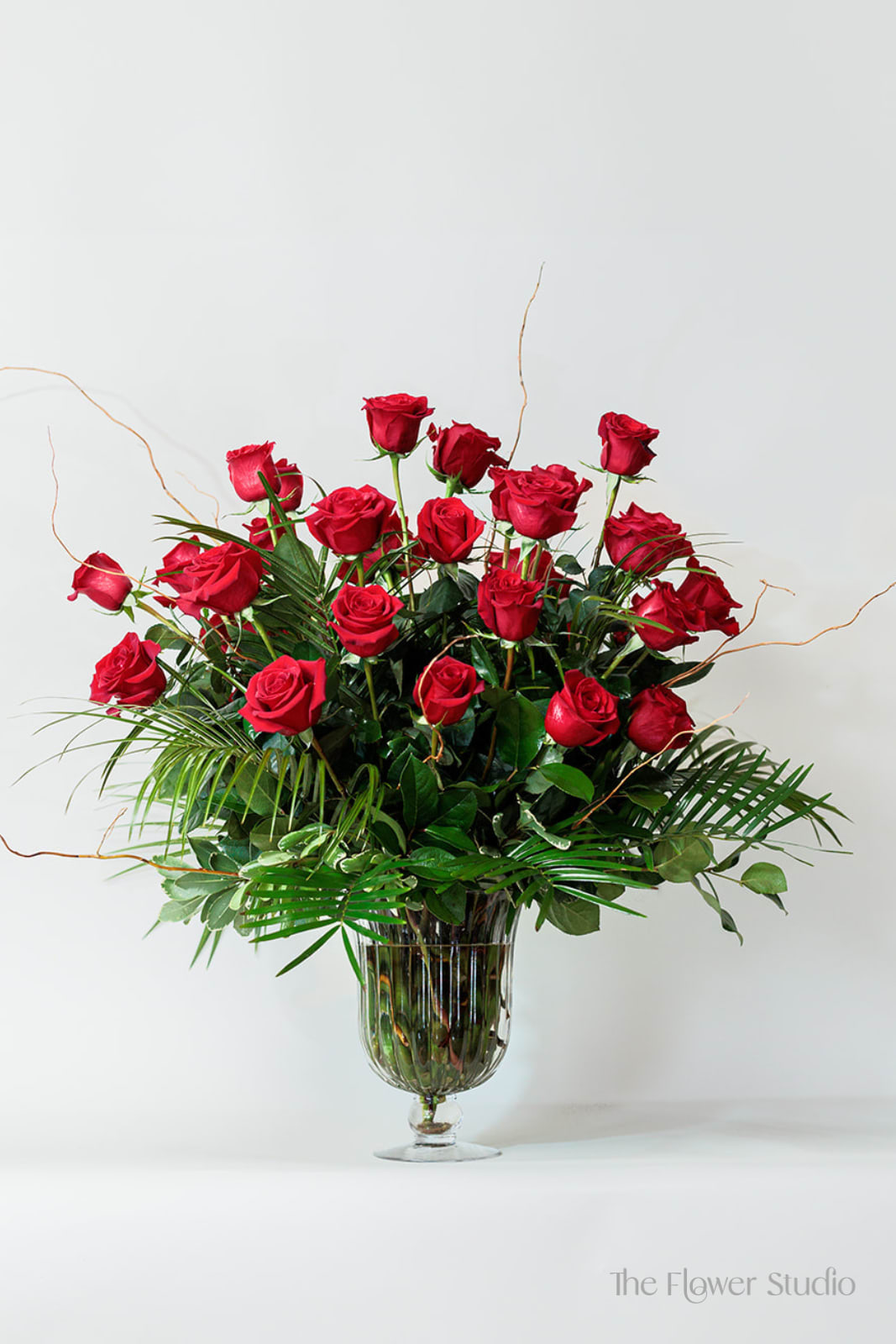Red roses arranged in a clear glass vase with greenery