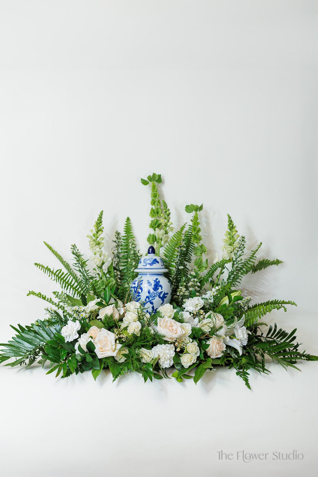 White roses and greenery arranged around a blue-and-white ceramic urn
