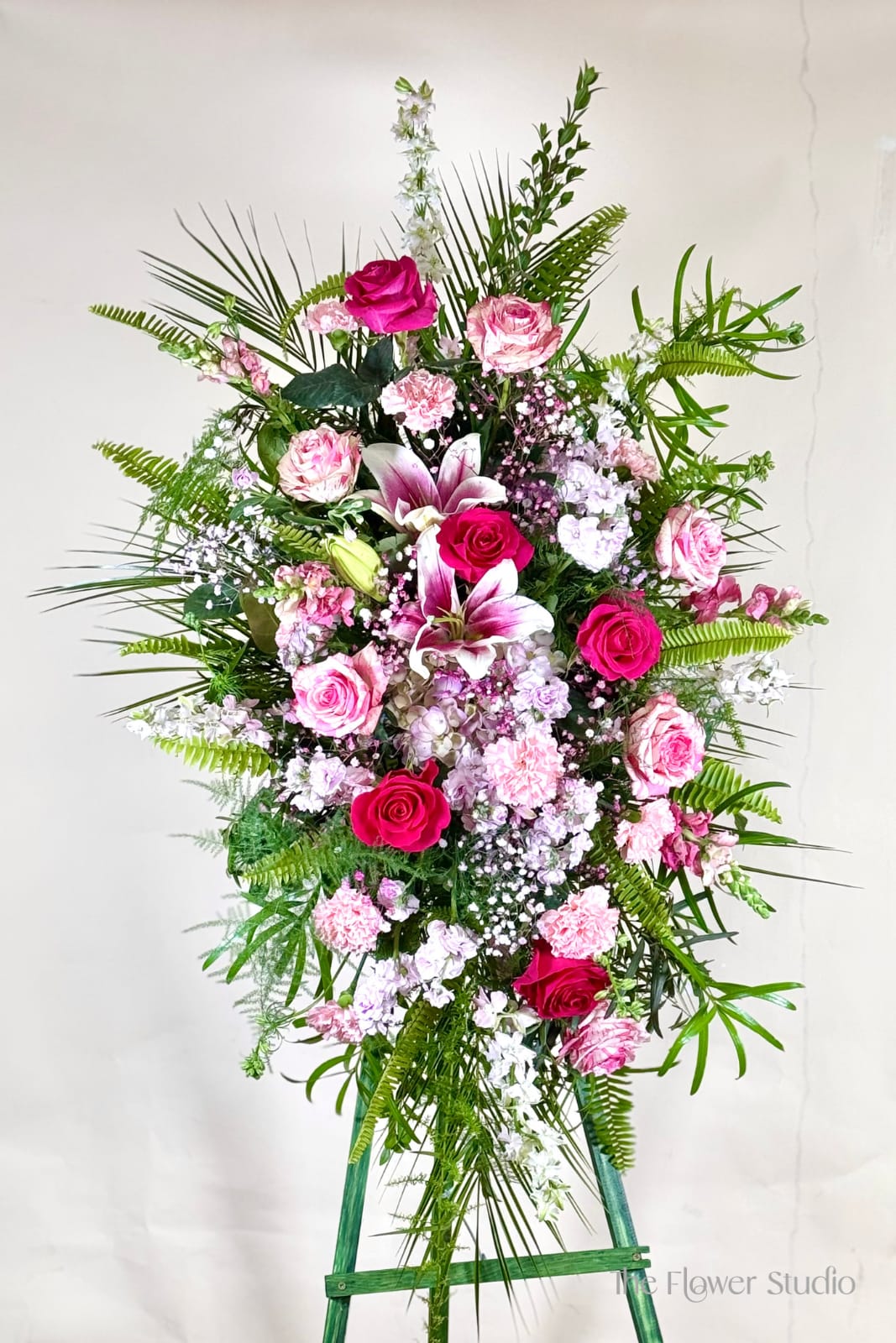 Tall standing floral spray with pink roses, lilies, and carnations on an easel