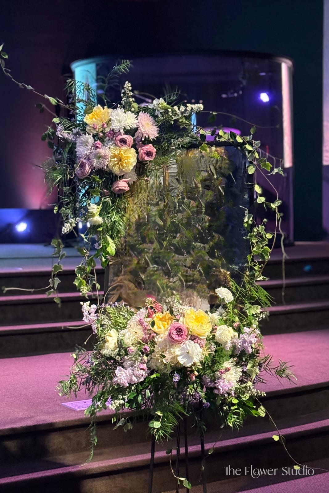Large floral arrangement with pastel blooms and trailing greenery on a stand