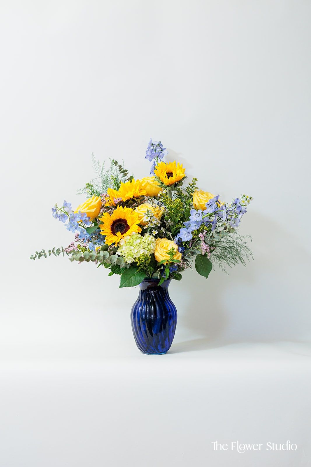 Yellow sunflowers and roses in a blue glass vase